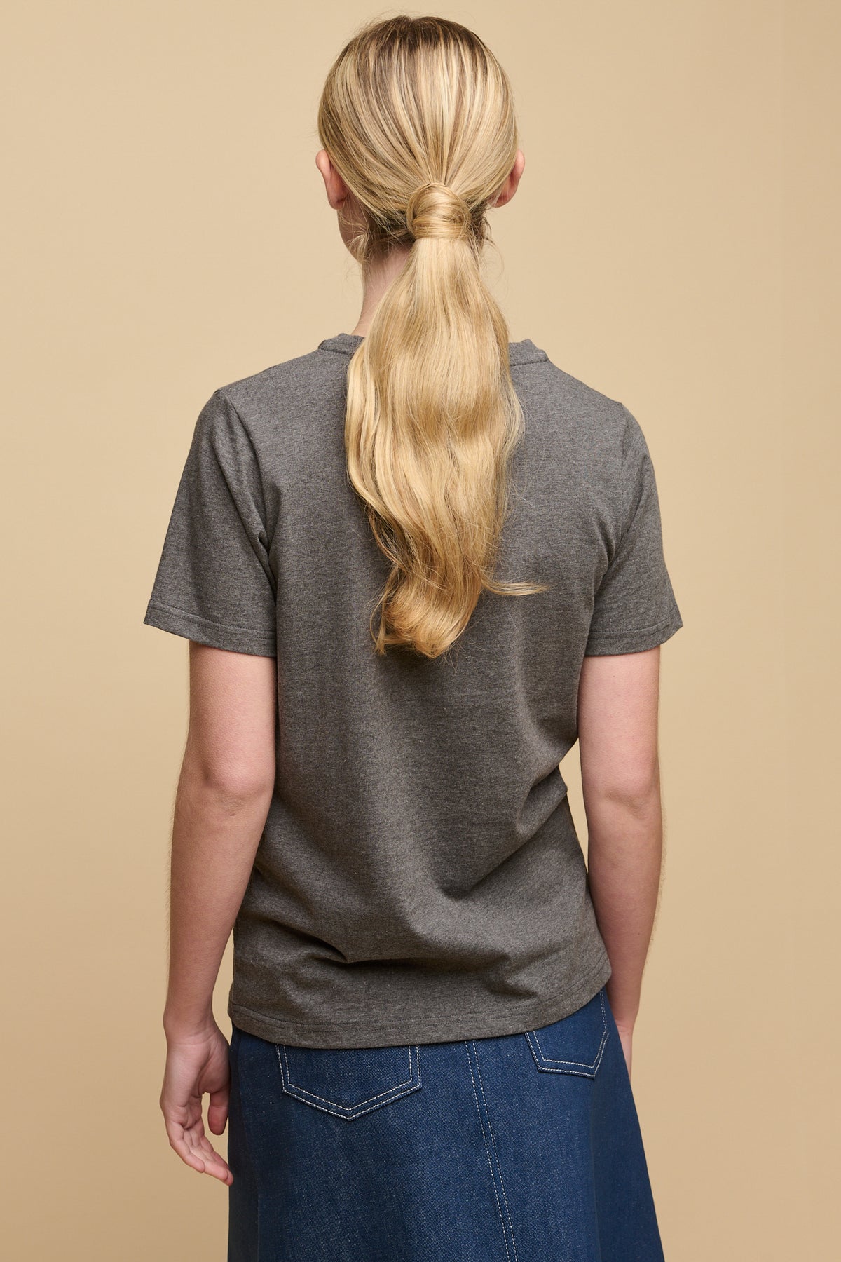 The back of female with long blonde hair tied back into low ponytail wearing short sleeve t shirt in charcoal