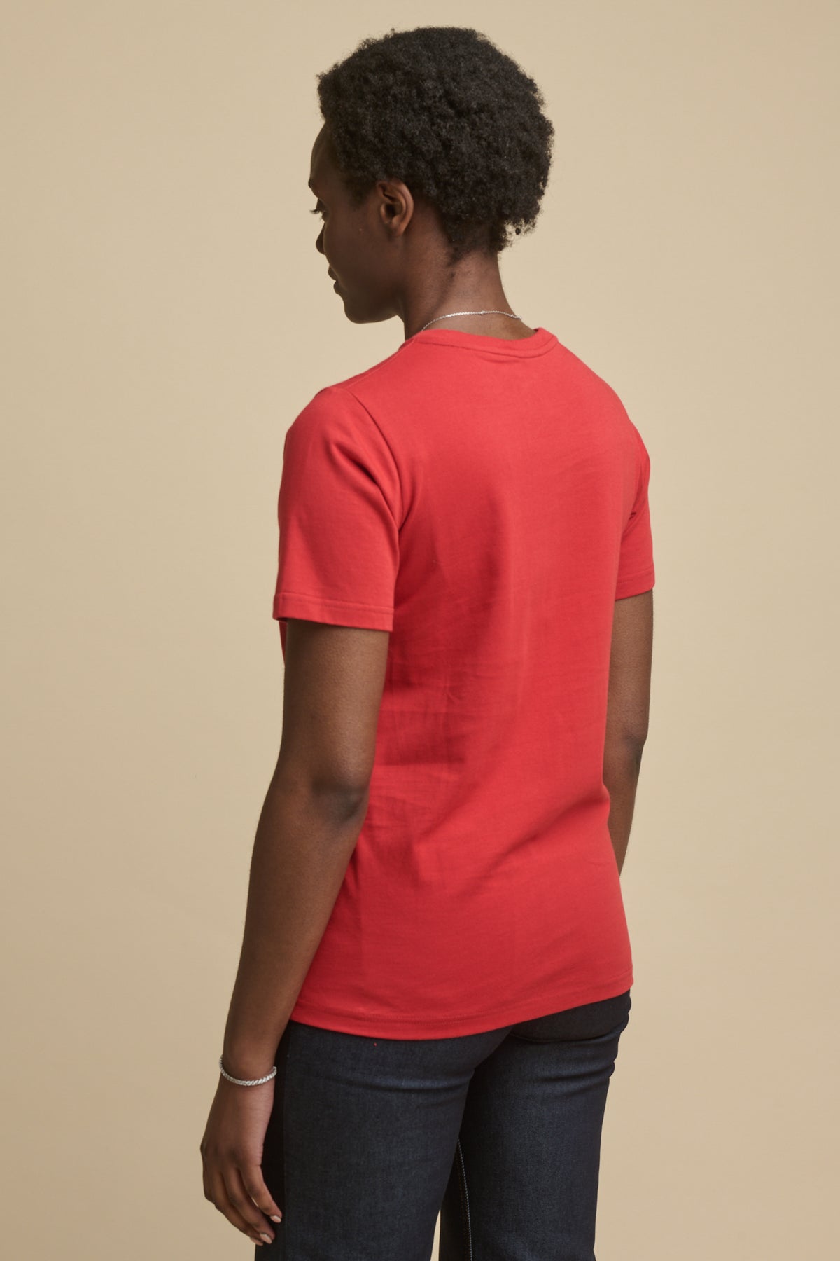 Thigh up image of the front of female in short sleeve t shirt in crimson paired with indigo jeans