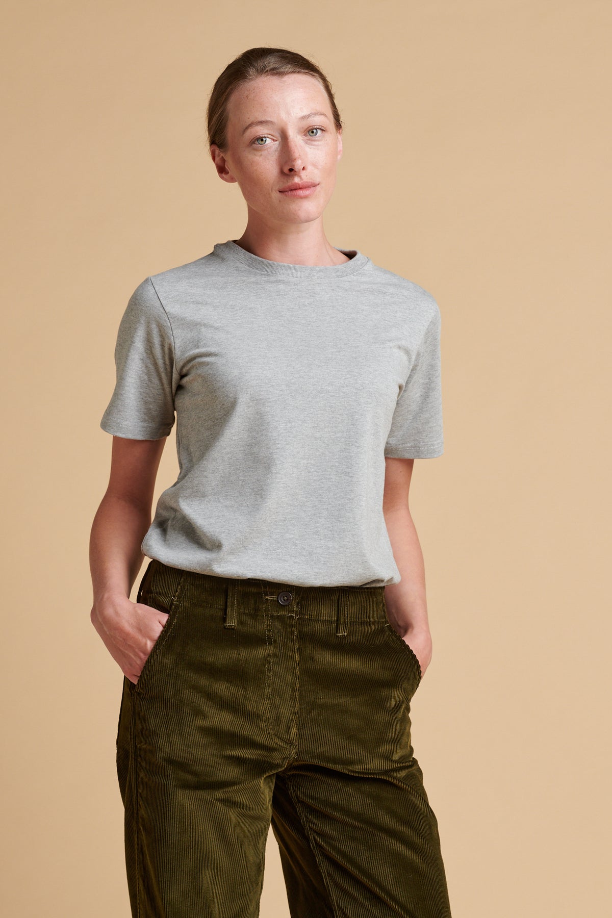 Female wearing short sleeve t shirt in grey marl tucked into corduroy work trousers in olive.