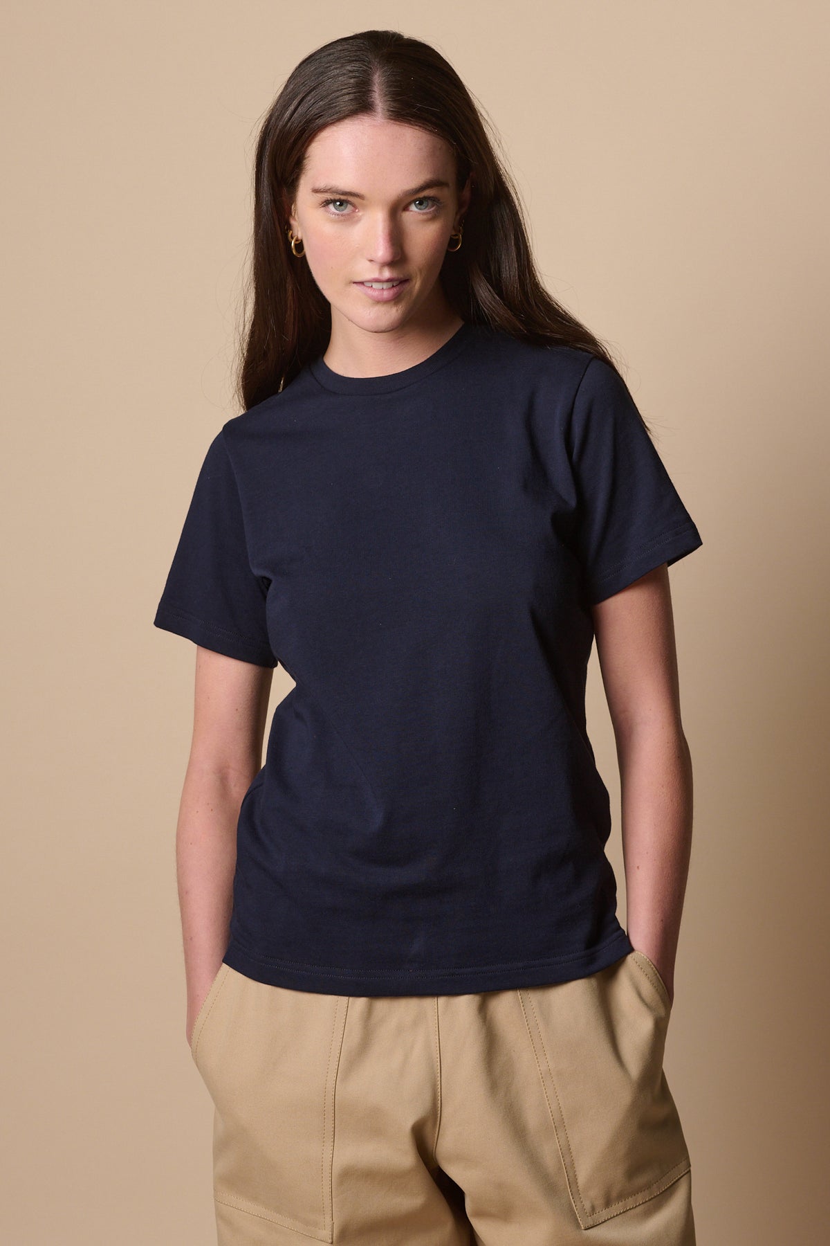 Thigh up image of female wearing short sleeve t shirt in navy with hands in pockets of camerawoman trousers in putty