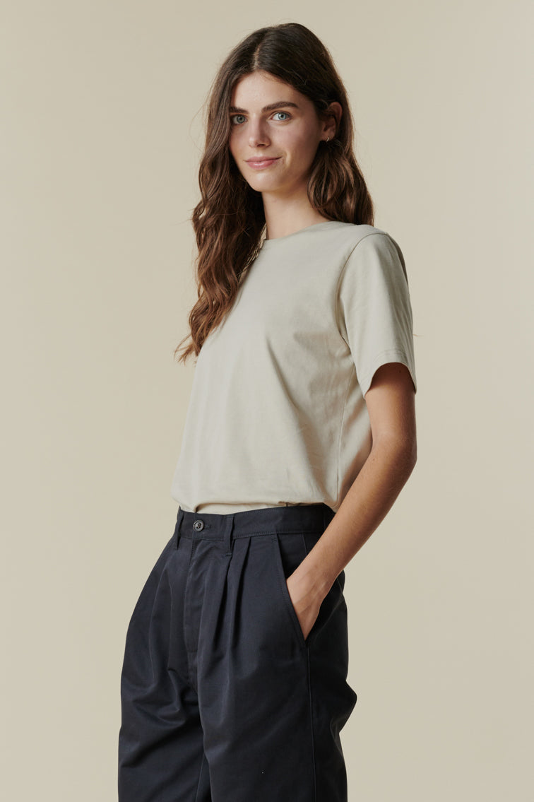 Brunette female wearing short sleeve t shirt in stone paired with pleated trousers in navy