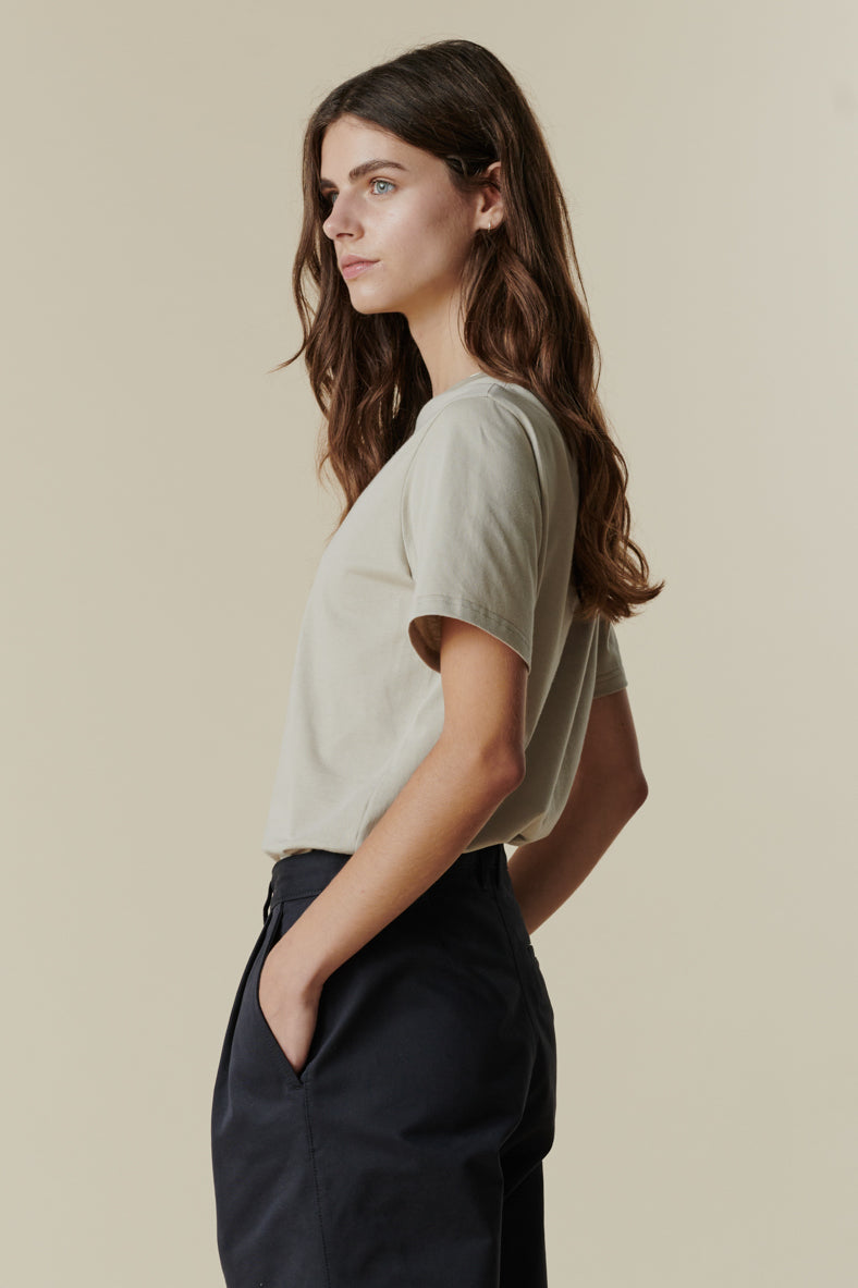 Thigh up image of female wearing short sleeve t shirt in stone paired with pleated trousers in navy