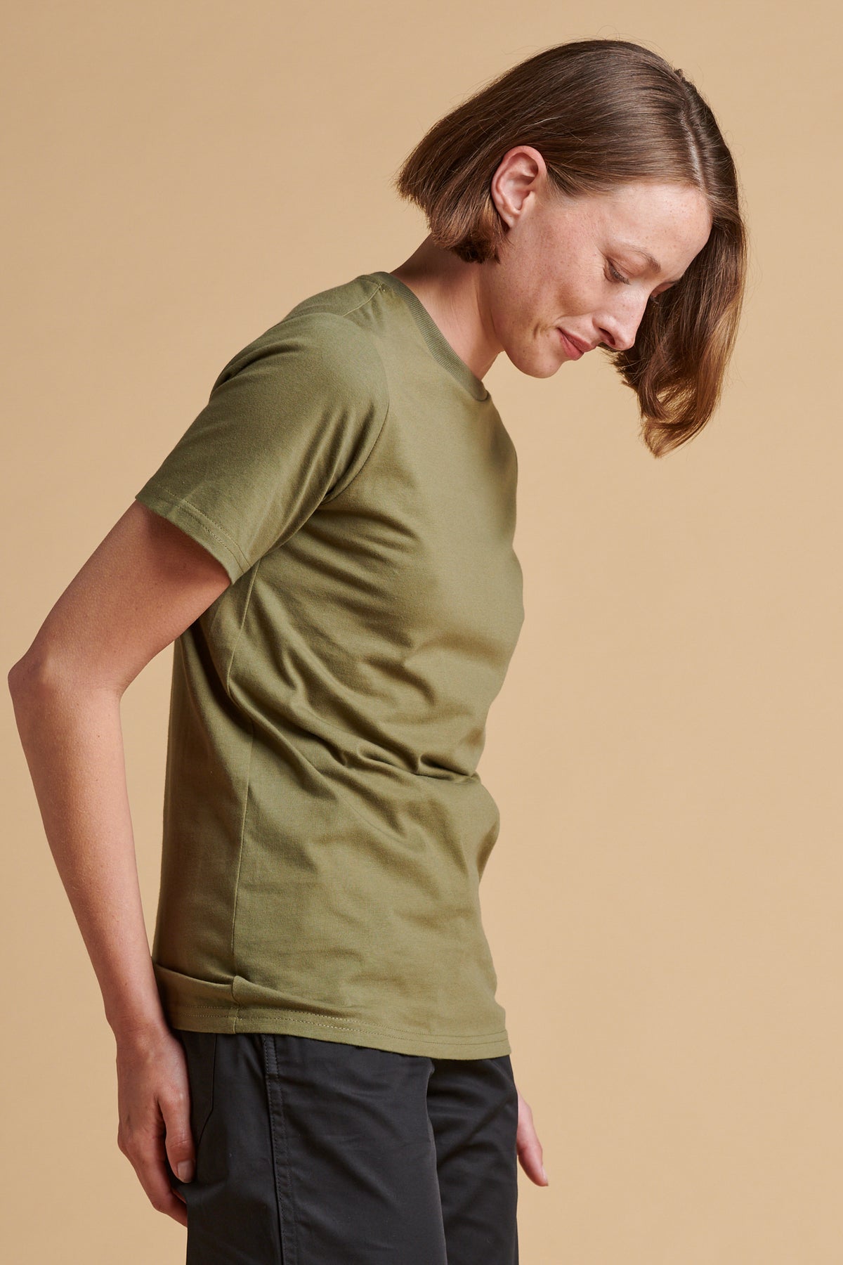 The side of female wearing short sleeve t shirt in olive.