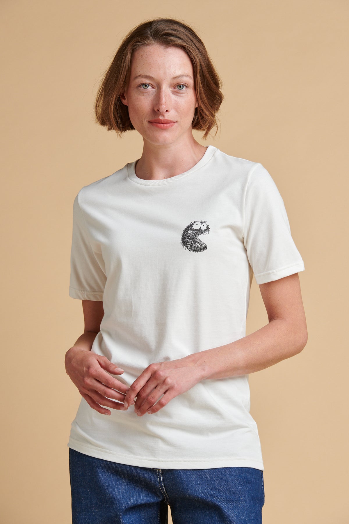 Female wearing a white t-shirt with a small graphic on a beige background.