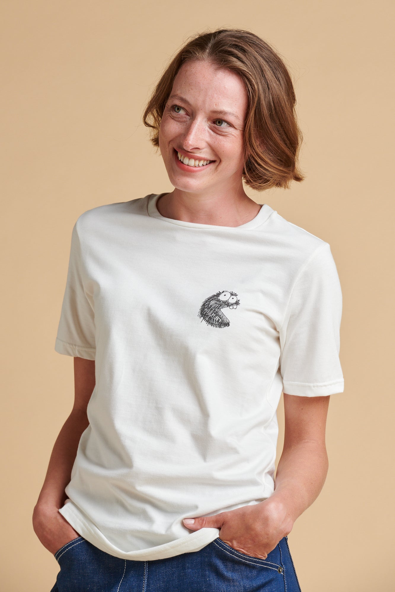 Female wearing a white t-shirt with a small graphic on a beige background.