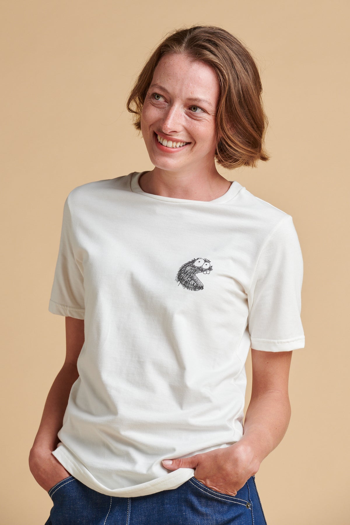 Female wearing a white t-shirt with a small graphic on a beige background.