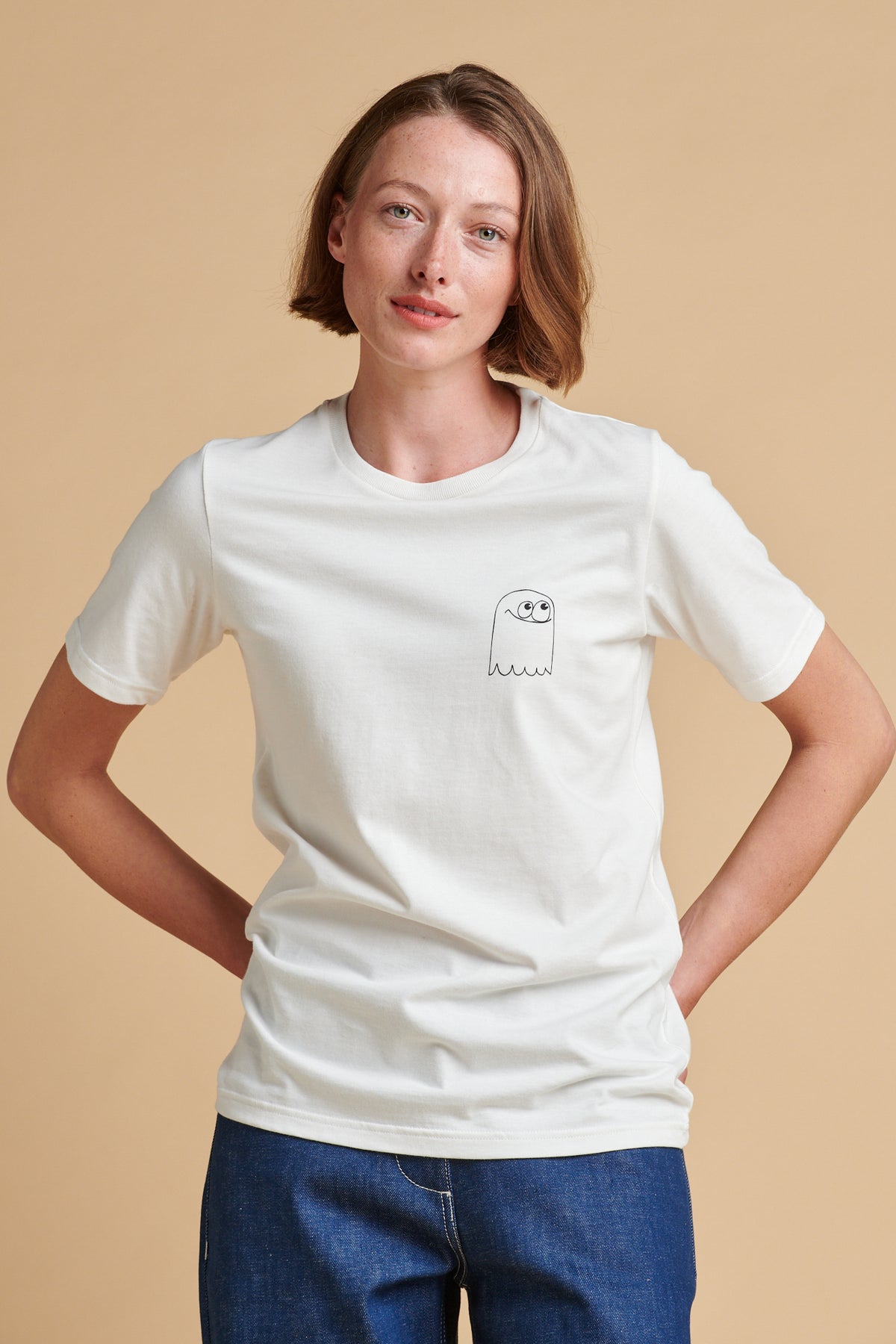 Person wearing a white t-shirt with a small graphic on a beige background