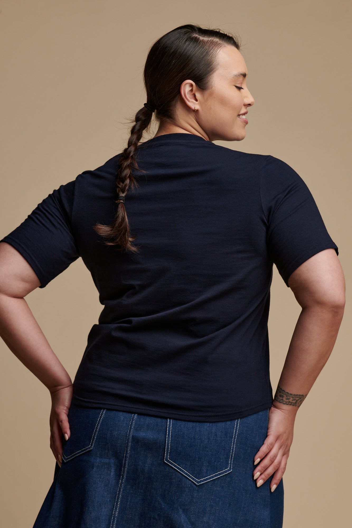 Thigh up of the back of female with her hand on her hips wearing short sleeve v neck t shirt in navy