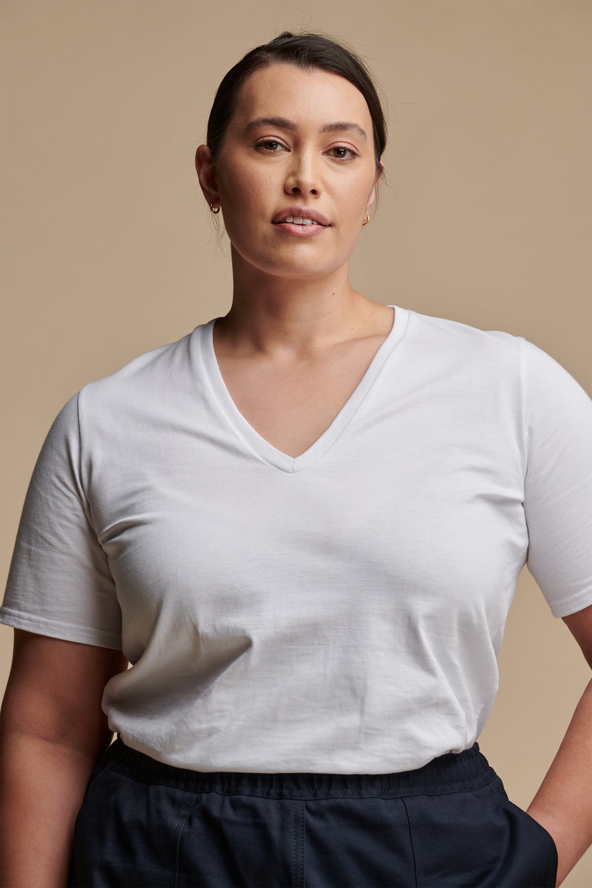 Hip up of female with brown hair tied back wearing short sleeve v neck t shirt tucked into camerawoman pants in navy.