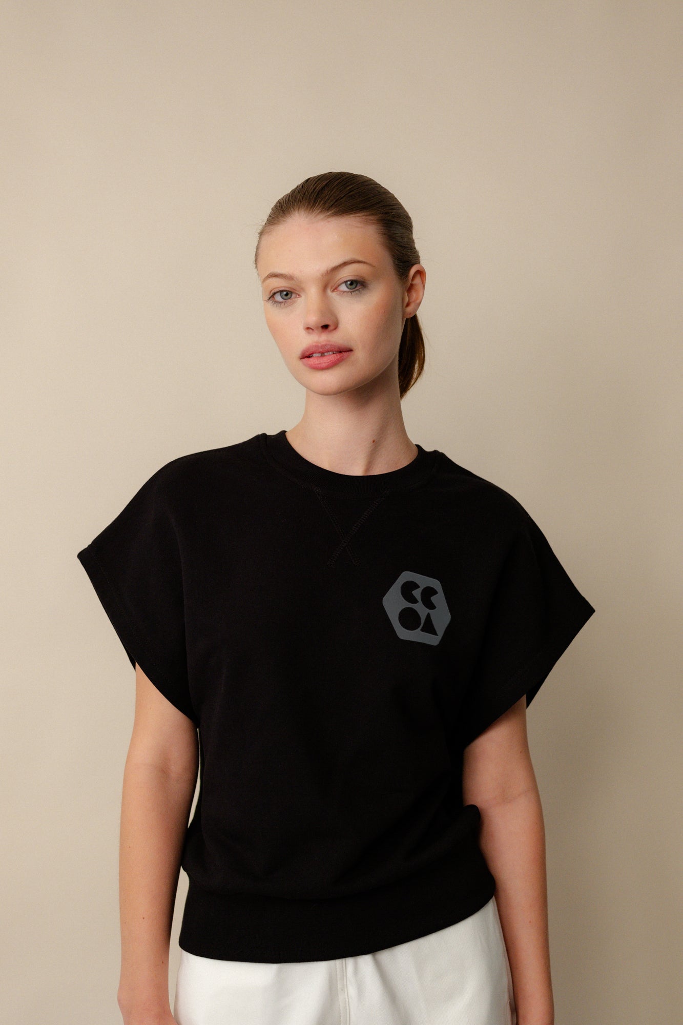Hip up image of white, brunette female wearing sleeveless sweatshirt plastic free in black. CCOA logo print