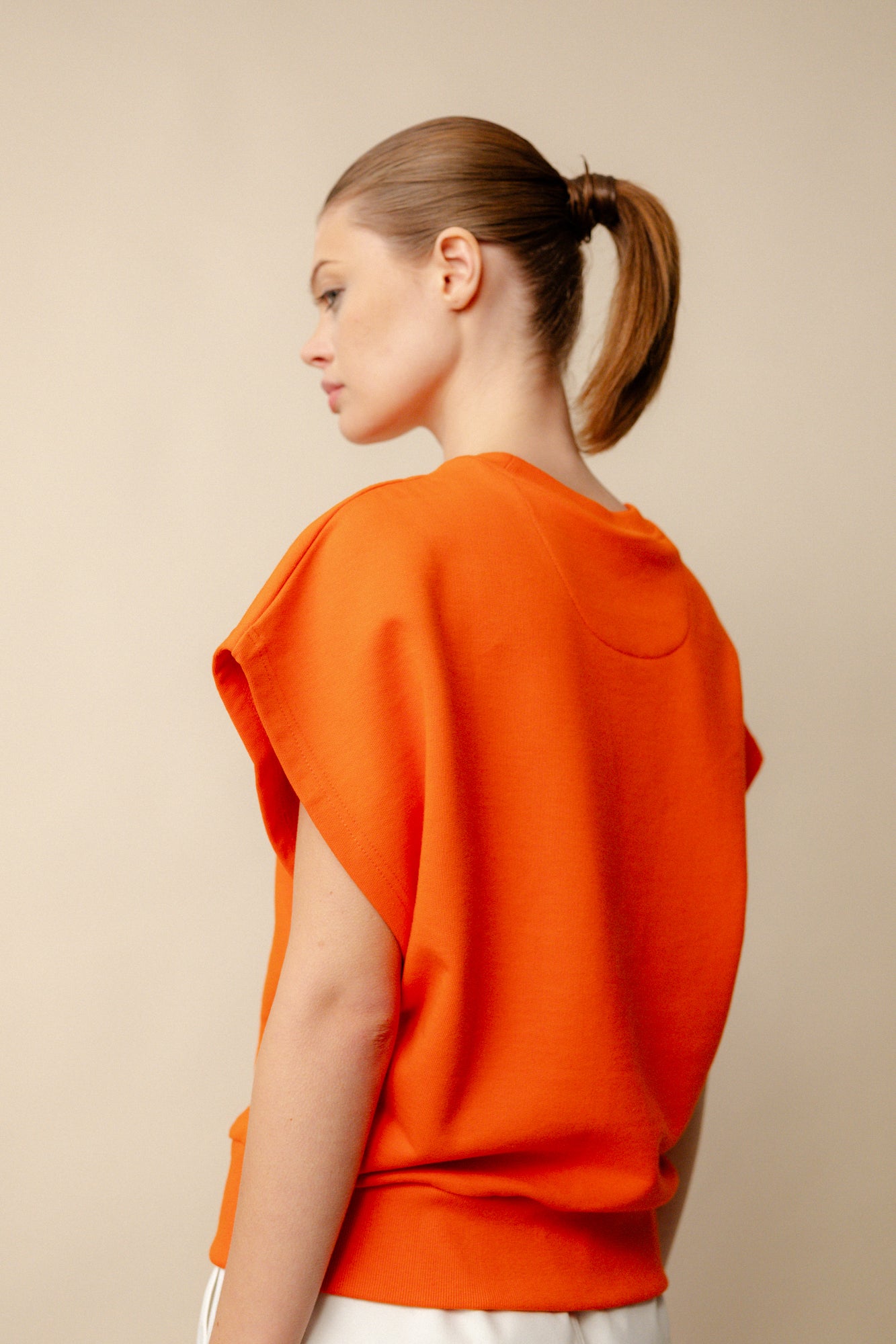Hip up image of white, brunette female from behind wearing sleeveless sweatshirt plastic free in flame red. White CCOA logo print