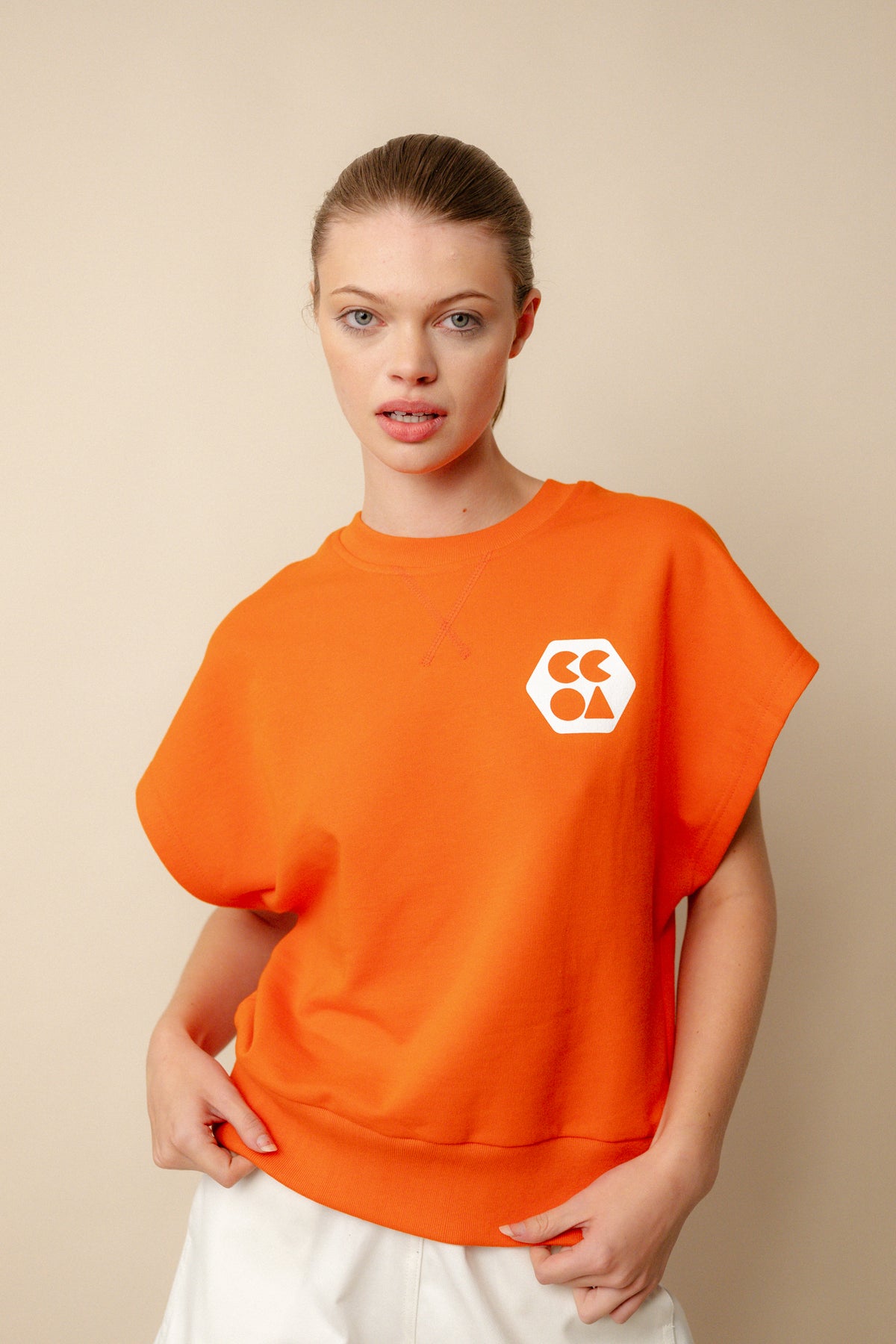 Hip up image of white, brunette female wearing sleeveless sweatshirt plastic free in flame red. White CCOA logo print