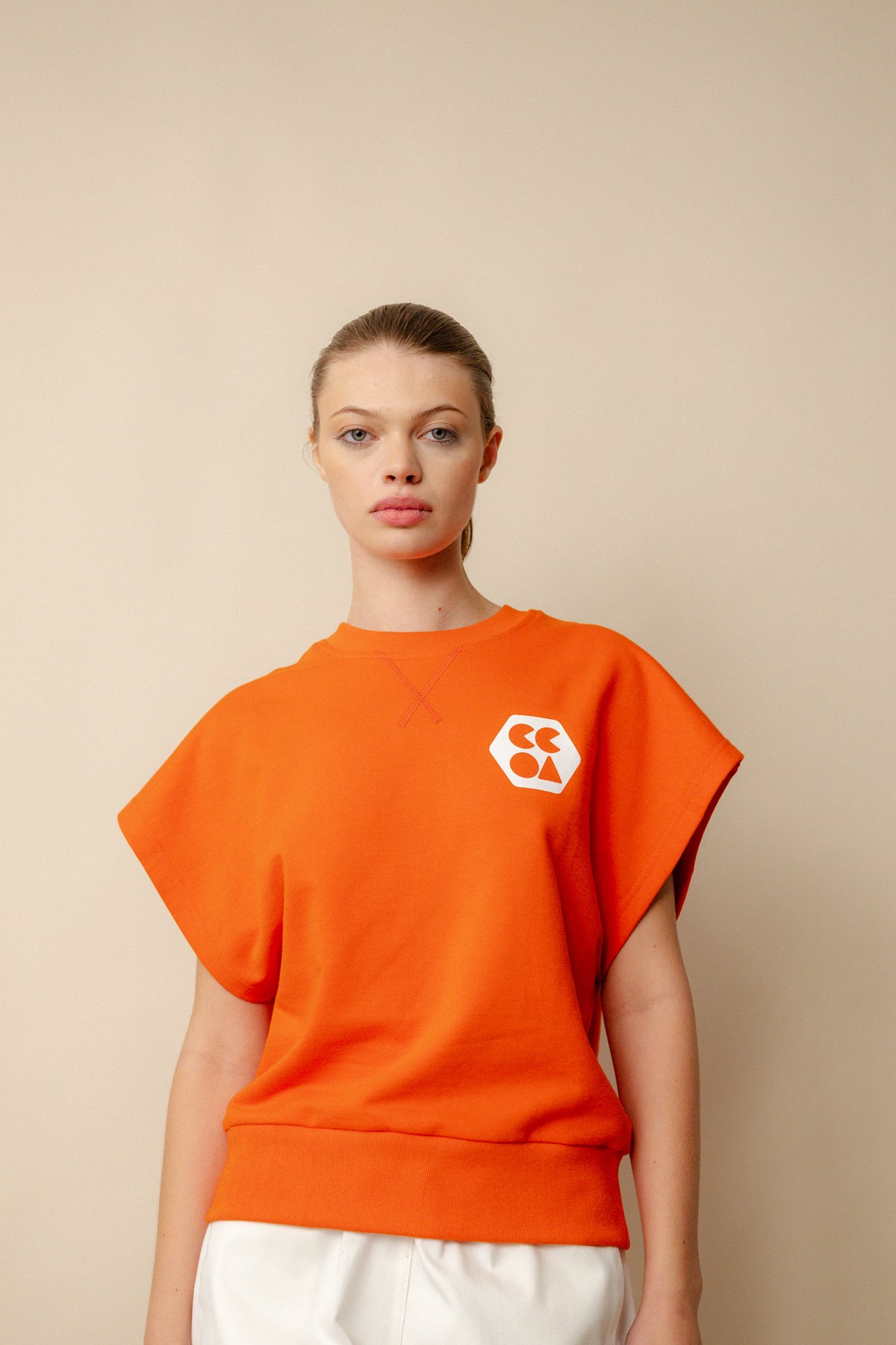 Hip up image of white, brunette female wearing sleeveless sweatshirt plastic free in flame red. White CCOA logo print