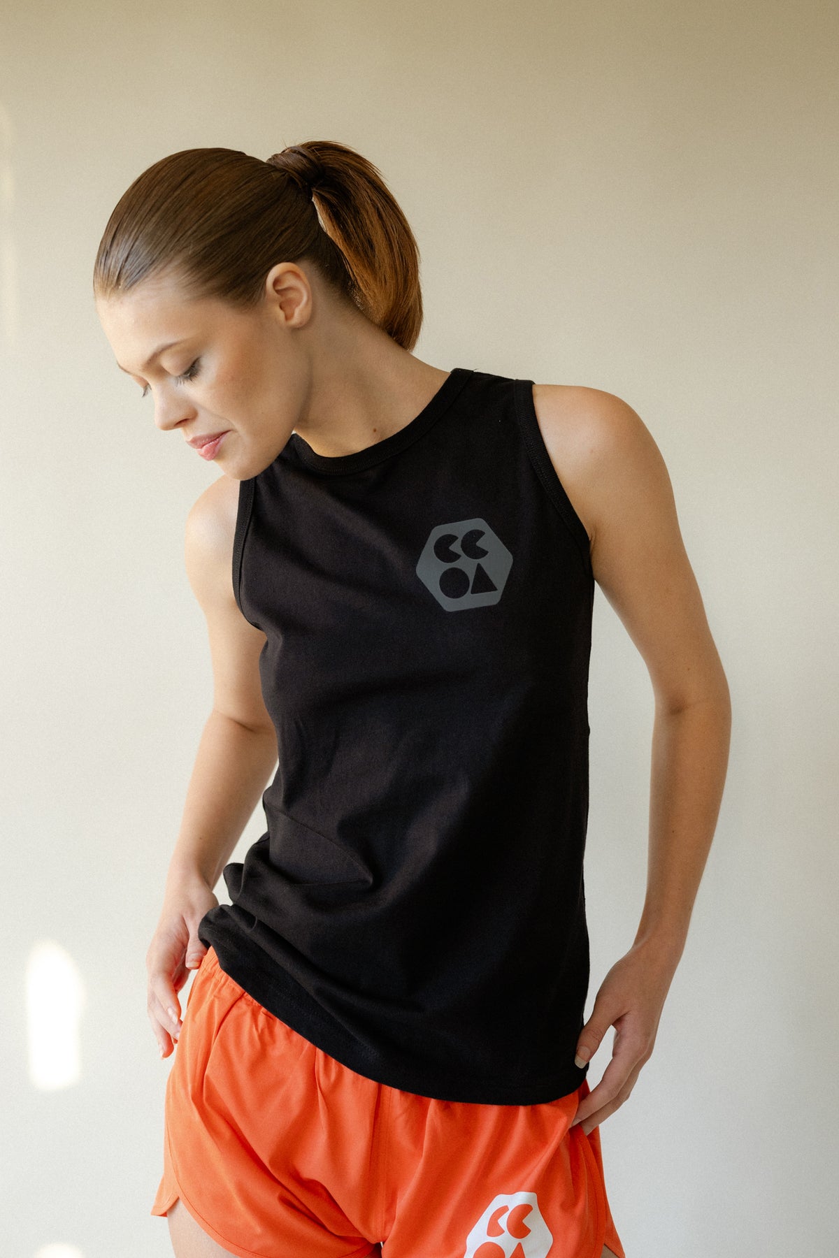 
            Portrait of female looking down at her hip wearing sleeveless t shirt plastic free in black with CCOA logo