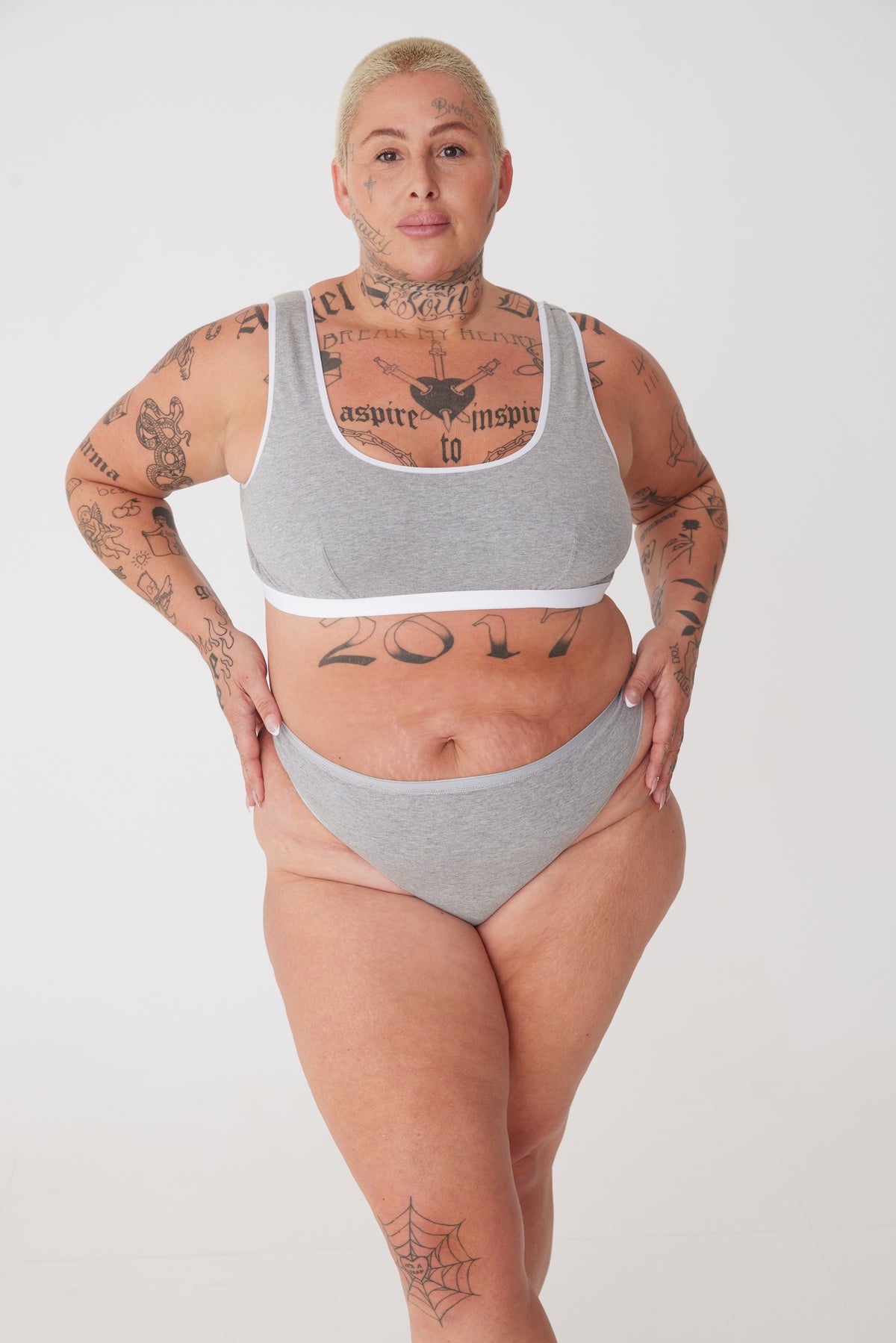 Plus sized female with short blonde hair wearing a soft jersey bra in grey with a matching low rise brief. All from Community Clothing.