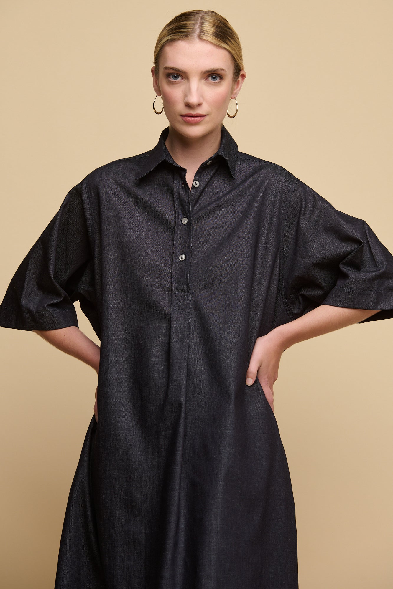 Thigh up image of female wearing straight denim dress in indigo with hands on hips