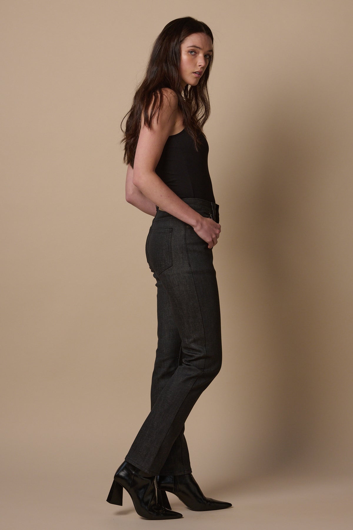 Full body image of the side of female wearing straight leg high rise jeans in black, worn with healed boots