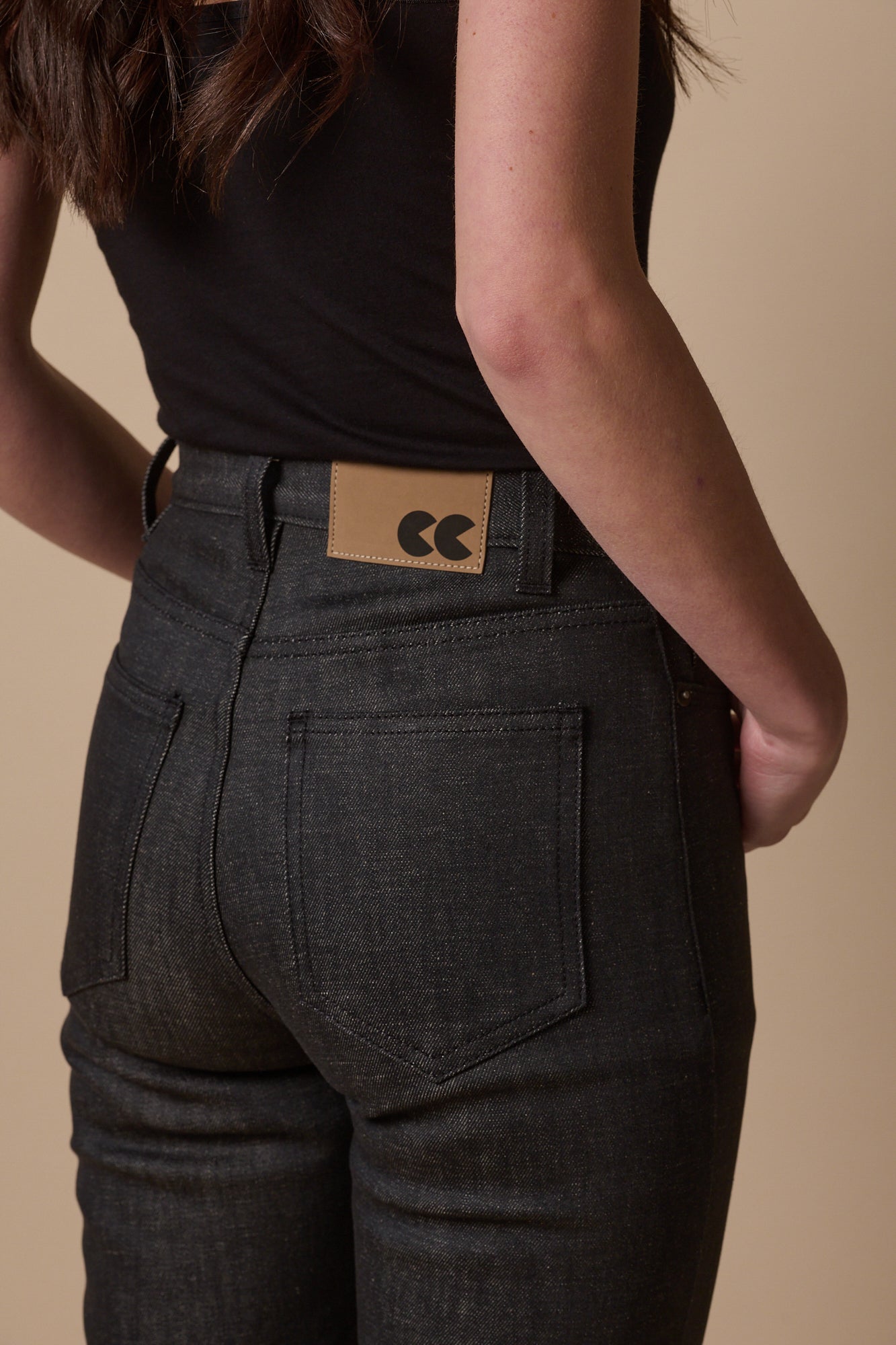 Close up of the back pockets of the straight leg high waist jeans in black. Jeans patch and belt loops on the waistband 