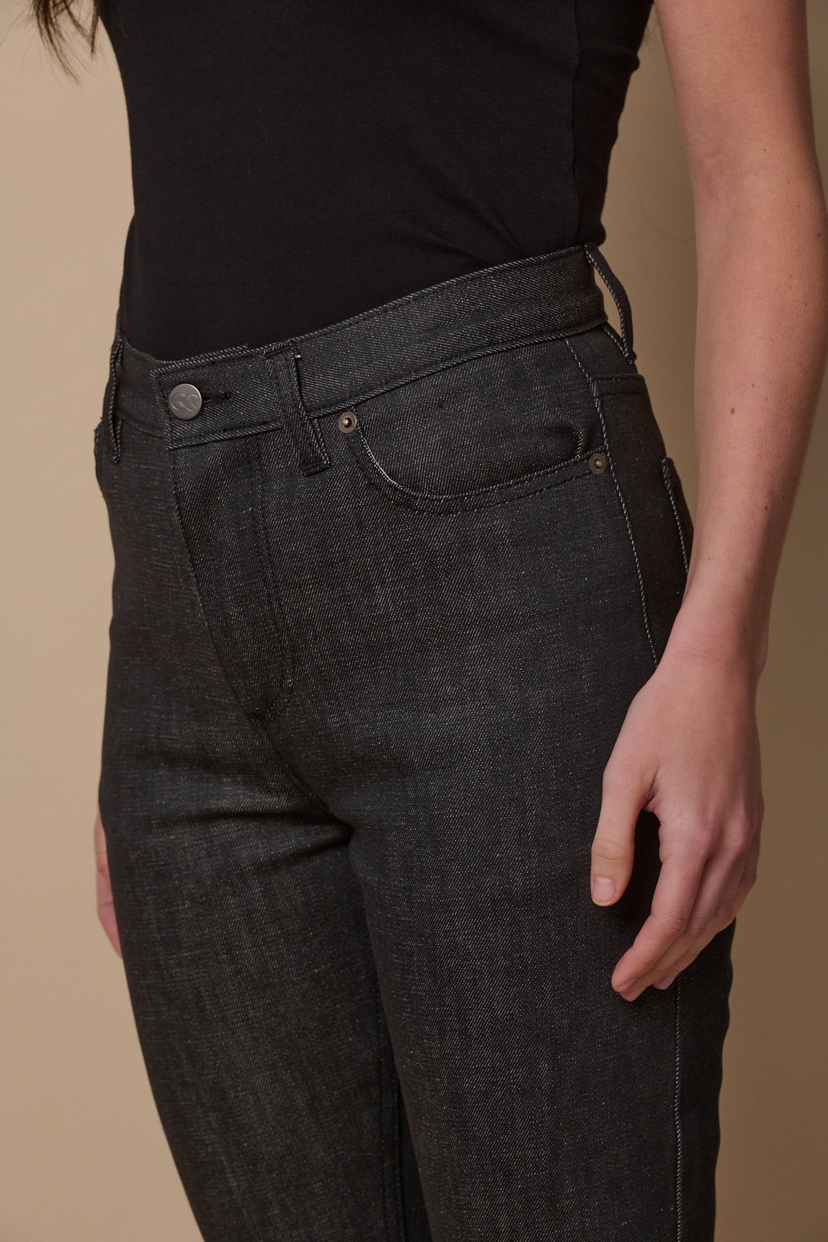 Close up image of female wearing straight leg high rise jeans in black with front pockets and belt loops