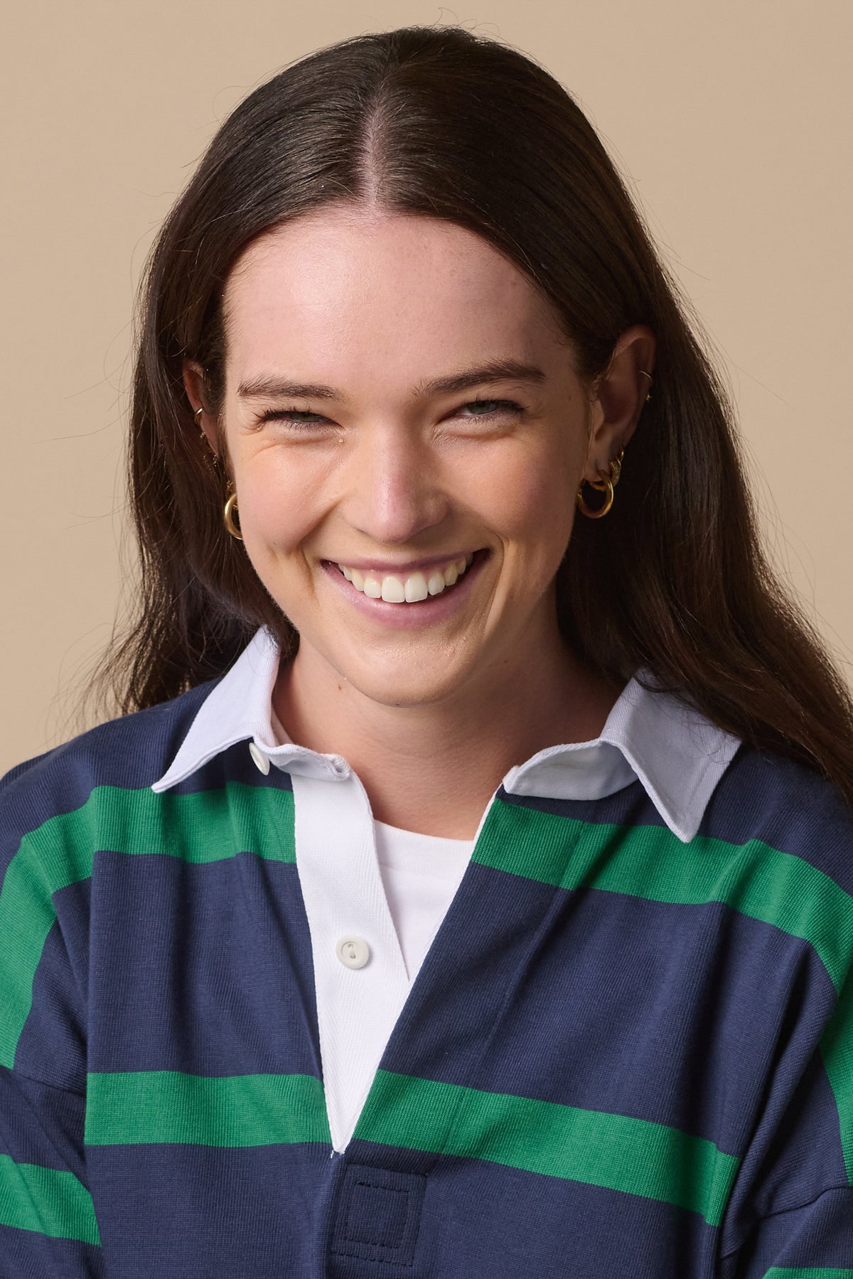 Portrait of smiley, white female wearing stripe rugby shirt in navy emerald with top buttons undone and cllar open showing white t shirt underneath