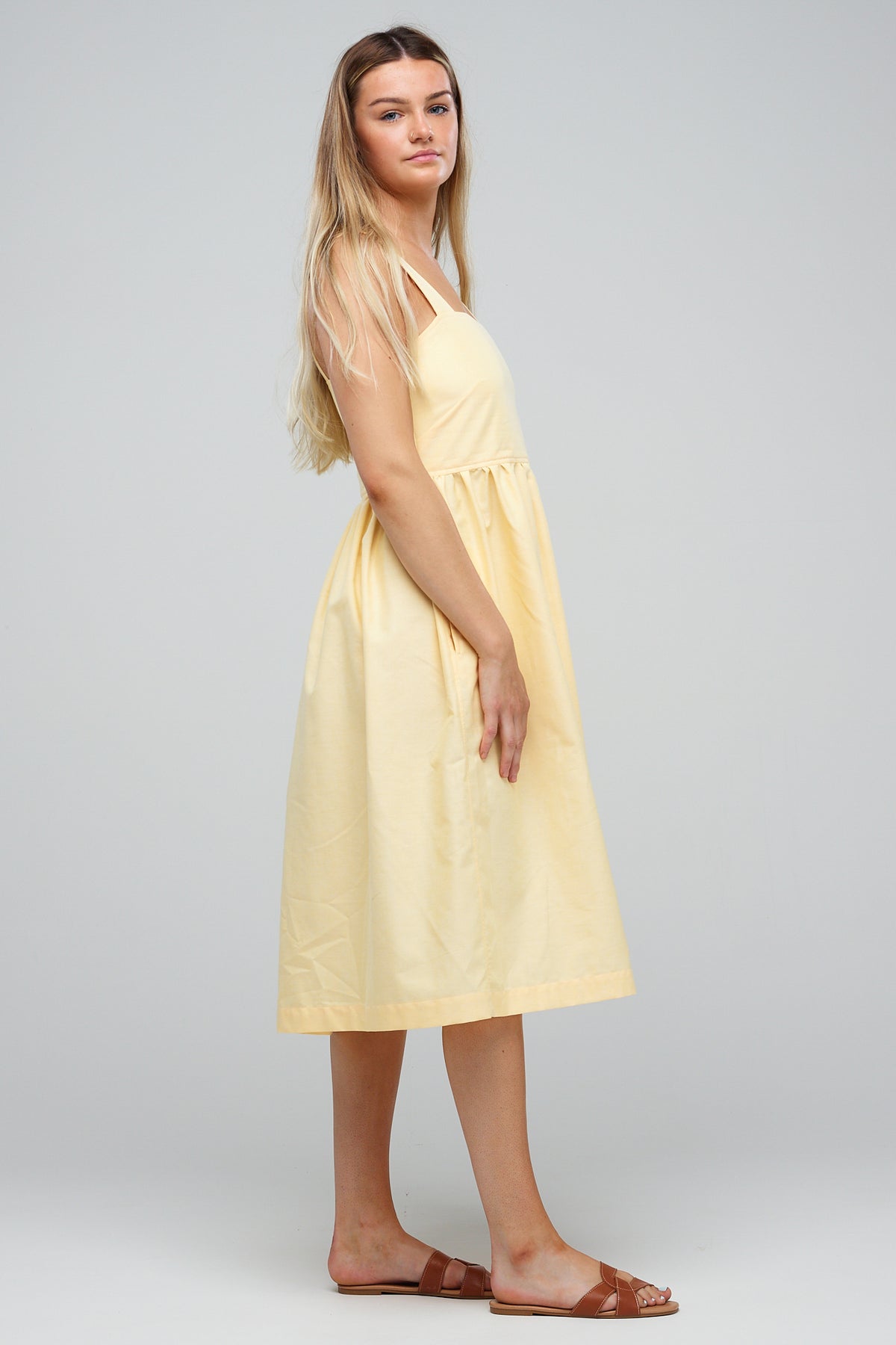 
            full body image of the side of female wearing sundress in lemon cotton oxford paired with brown sandals