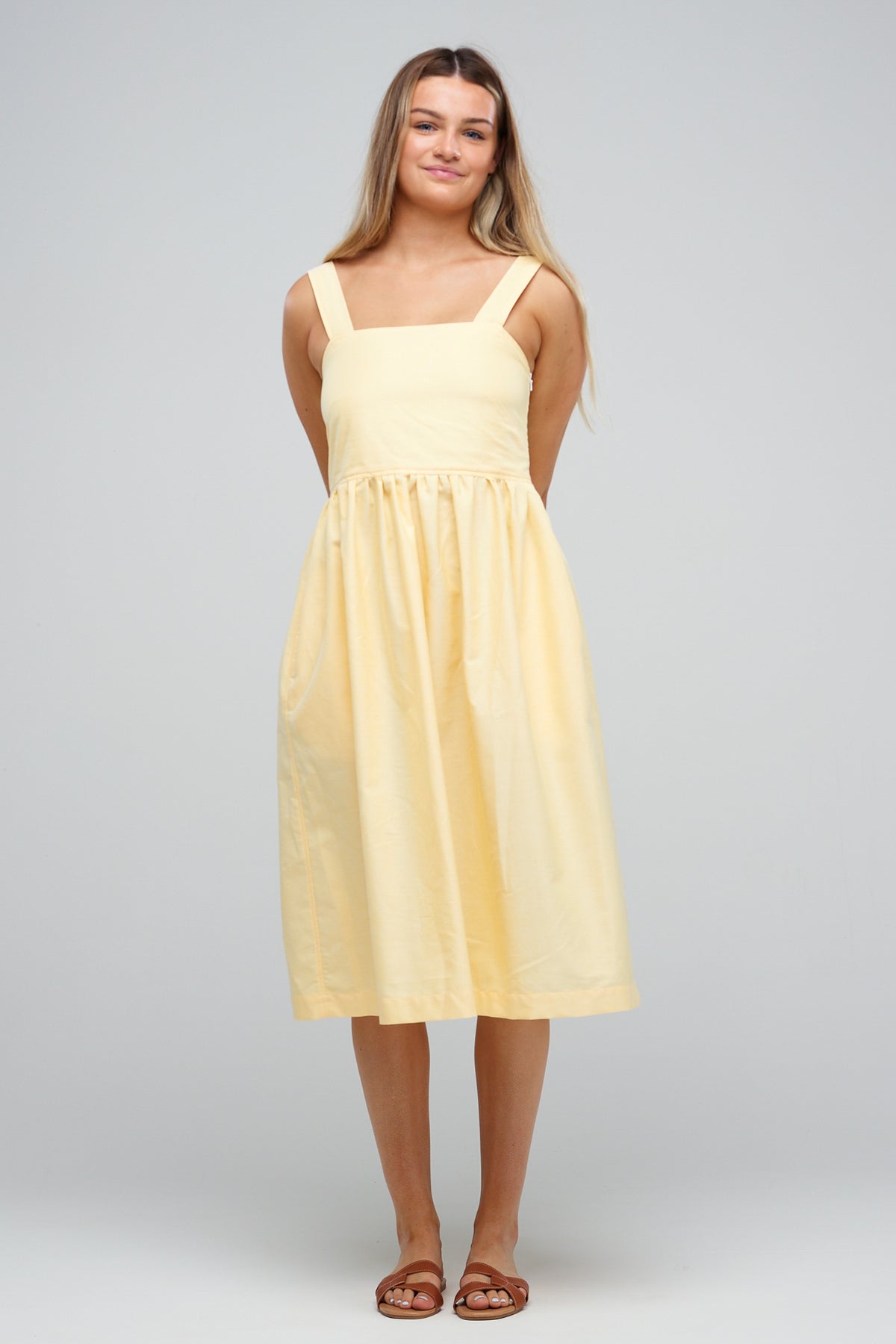 
            Full body image of female with long hair wearing sun dress in lemon cotton oxford with brown sandals