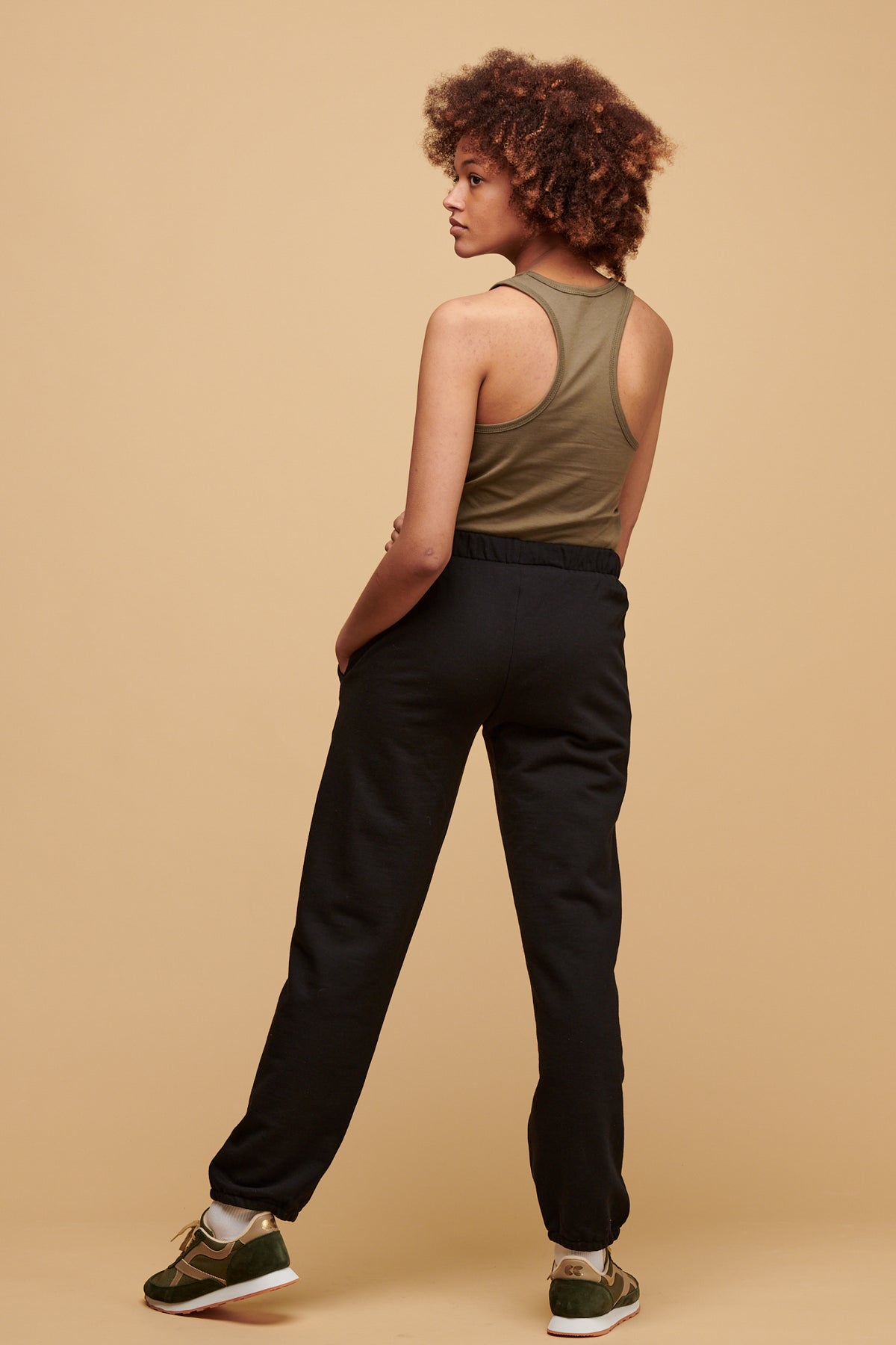 
            The back of female wearing 100% cotton sweatpants in black worn with plastic free racer back vest in olive tucked in.