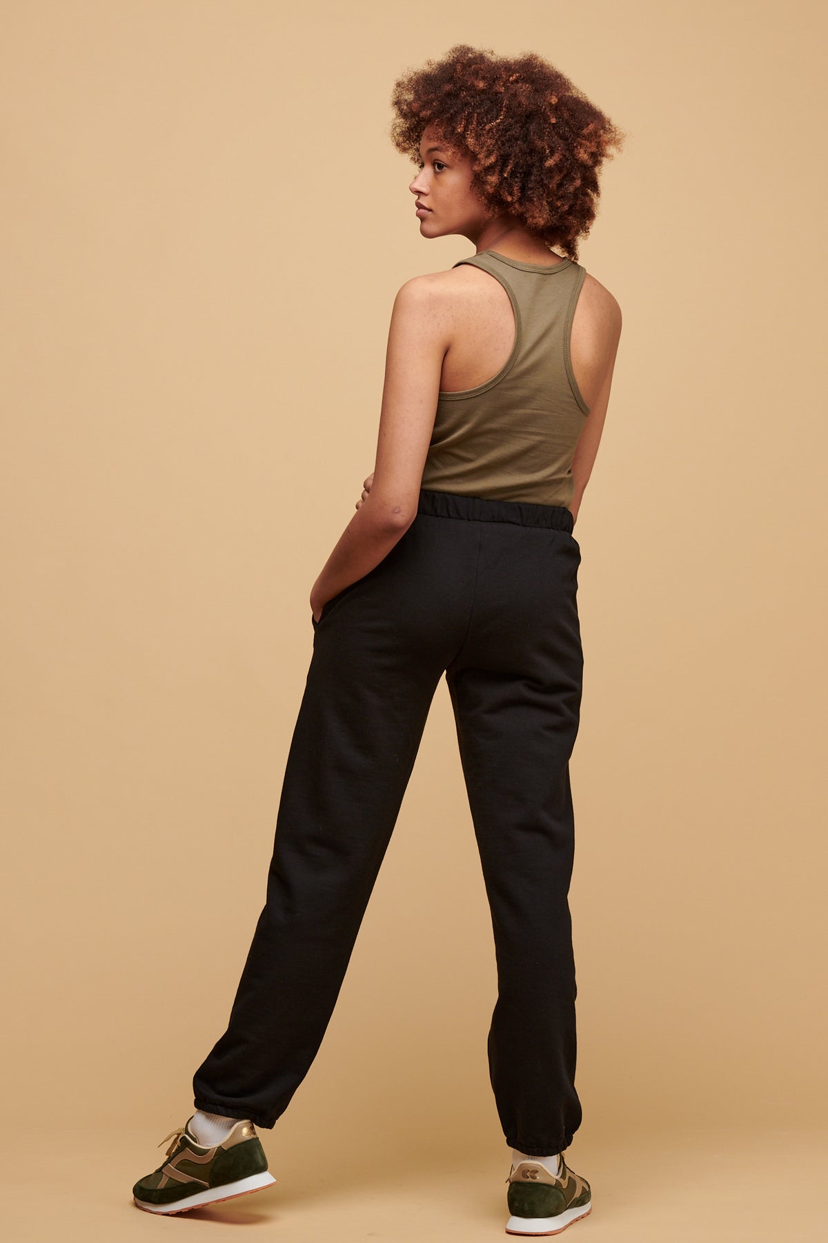 The back of female wearing 100% cotton sweatpants in black worn with plastic free racer back vest in olive tucked in.