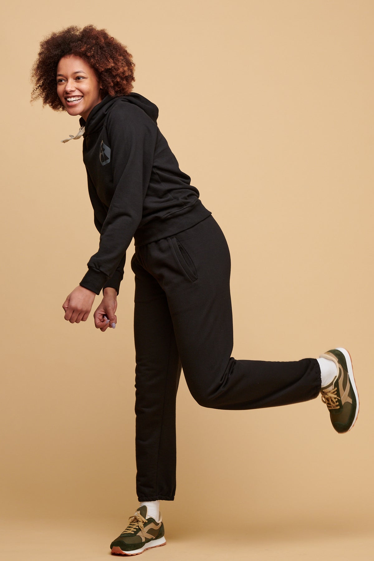 Smiley female kicking her leg back wearing black sweatpants in black paired with plastic free CCOA hooded sweatshirt in black