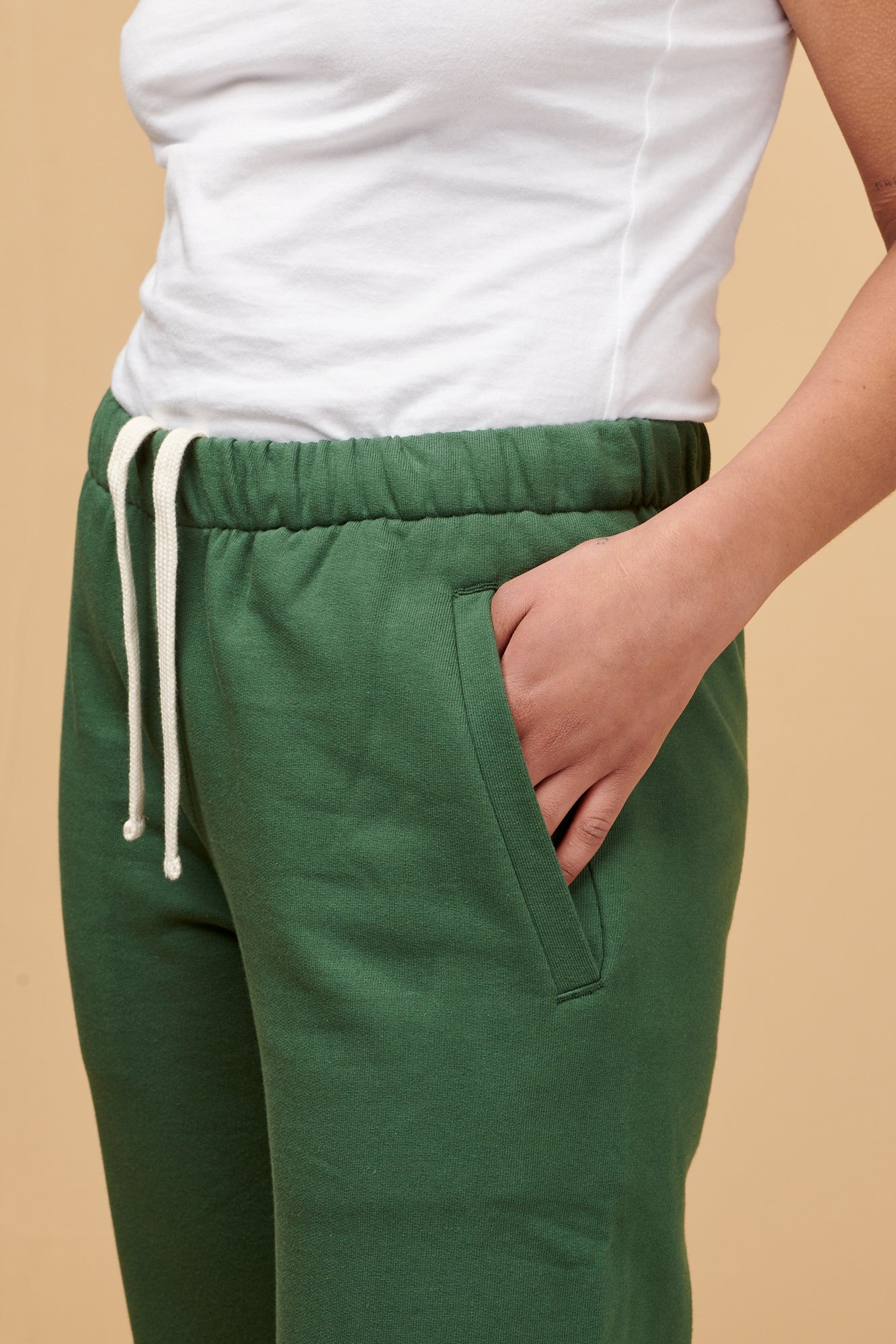 Close up of female wearing women's sweatpants in bottle green with her hand in the front pocket, elasticated waistband with adjustable ecru drawcord 