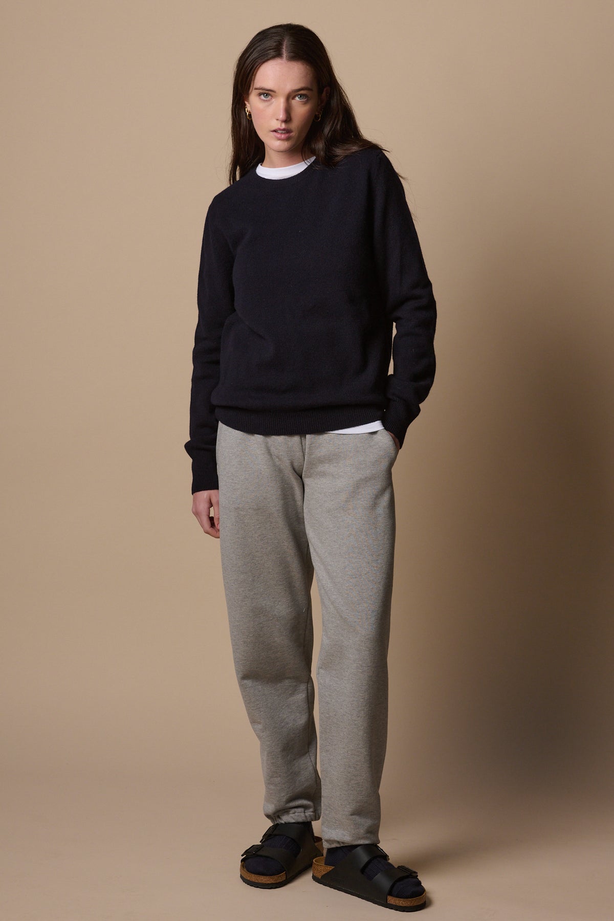 Brunette female wearing sweatpants in grey marl with hands in front pockets. Worn with lambswool crew neck in navy