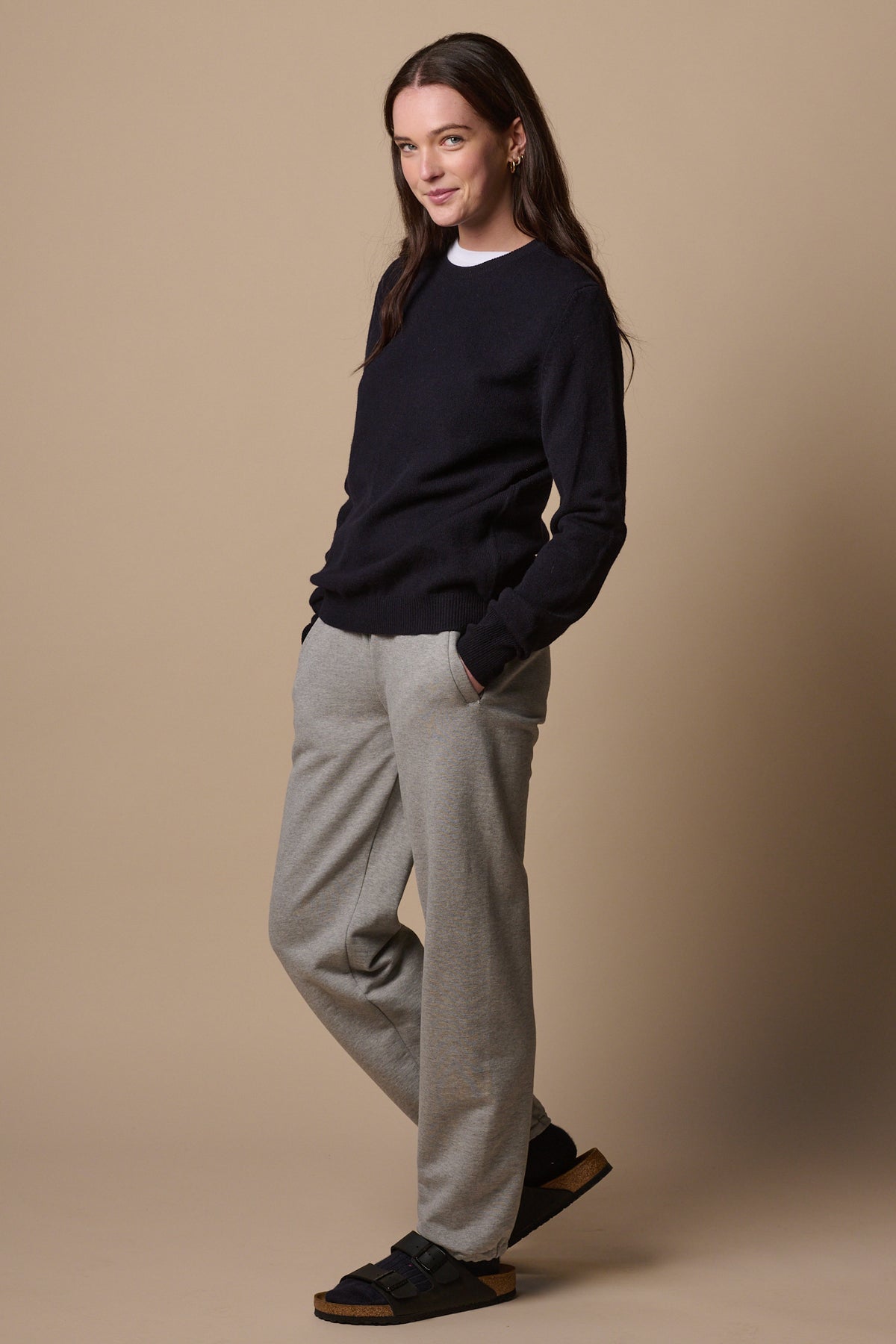 Brunette female wearing sweatpants in grey marl with hands in front pockets. Worn with lambswool crew neck in navy