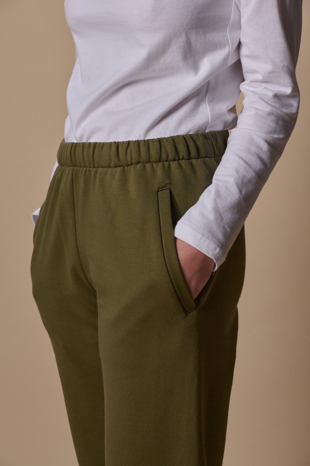 
            close up showing elasticated waistband of sweatpants in olive with two front pockets, model wearing long sleeve t shirt tucked in