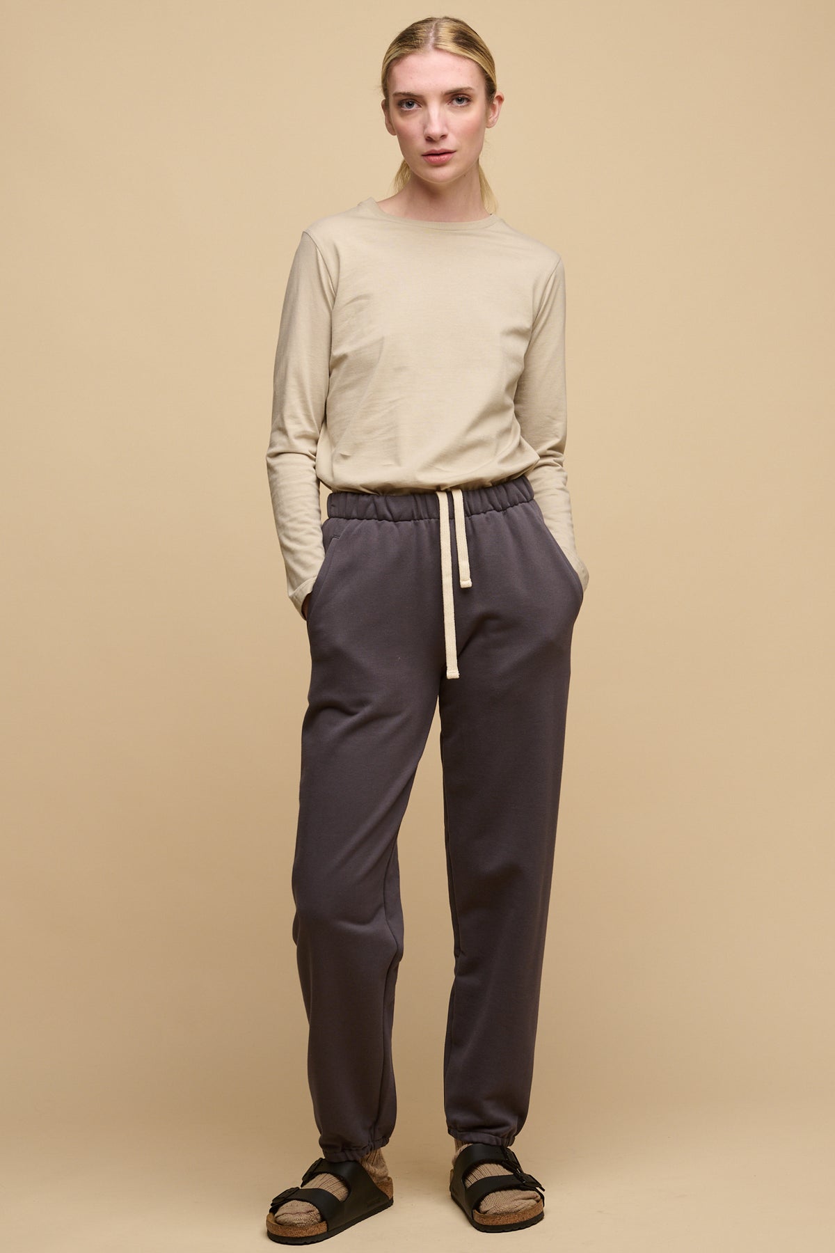 Full body image of the front of female wearing sweatpants in slate grey paired with long sleeve t shirt in stone