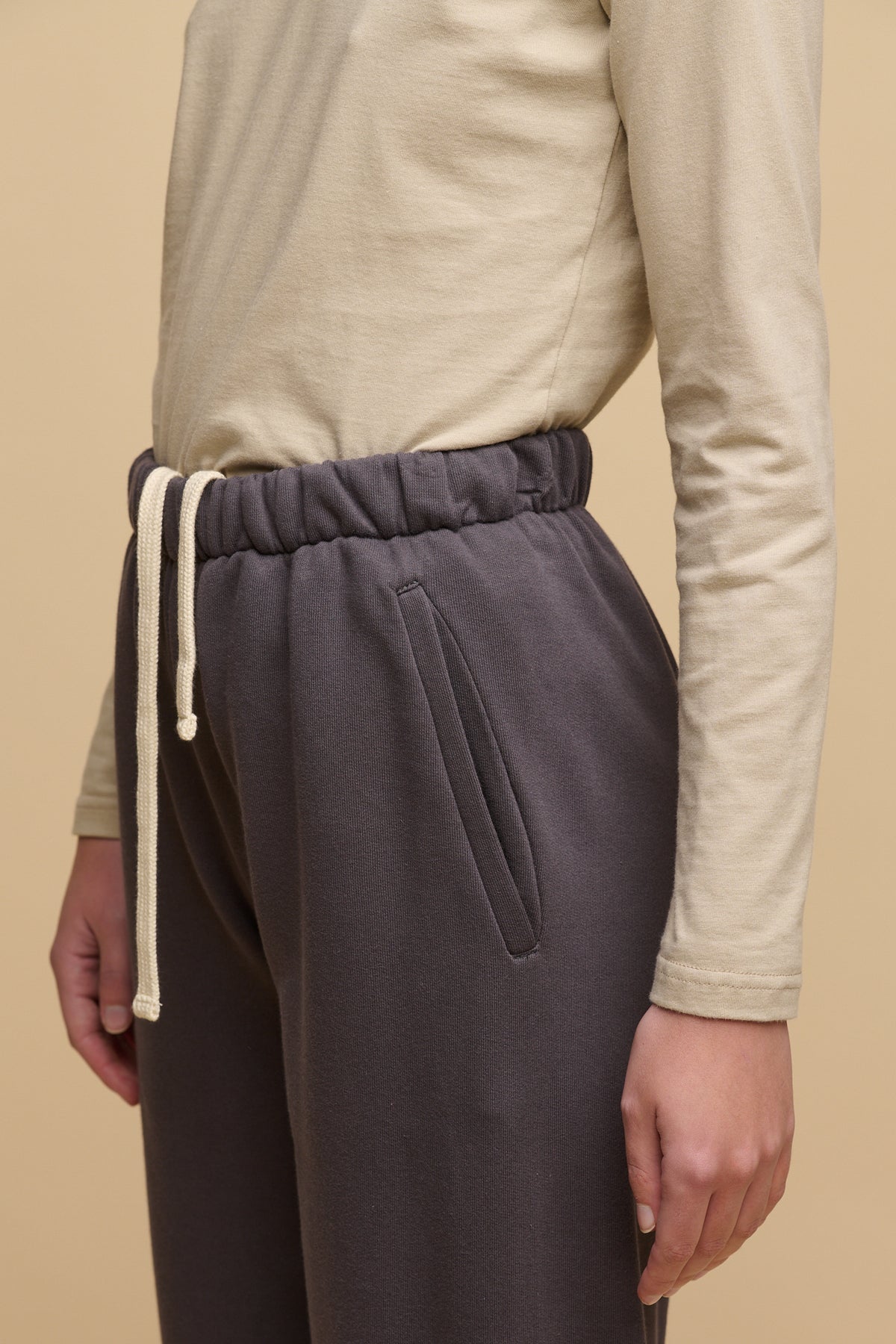 Close up image of the waistband and front pocket of sweatpants in slate grey. Adjustable waist with ecru drawstring.