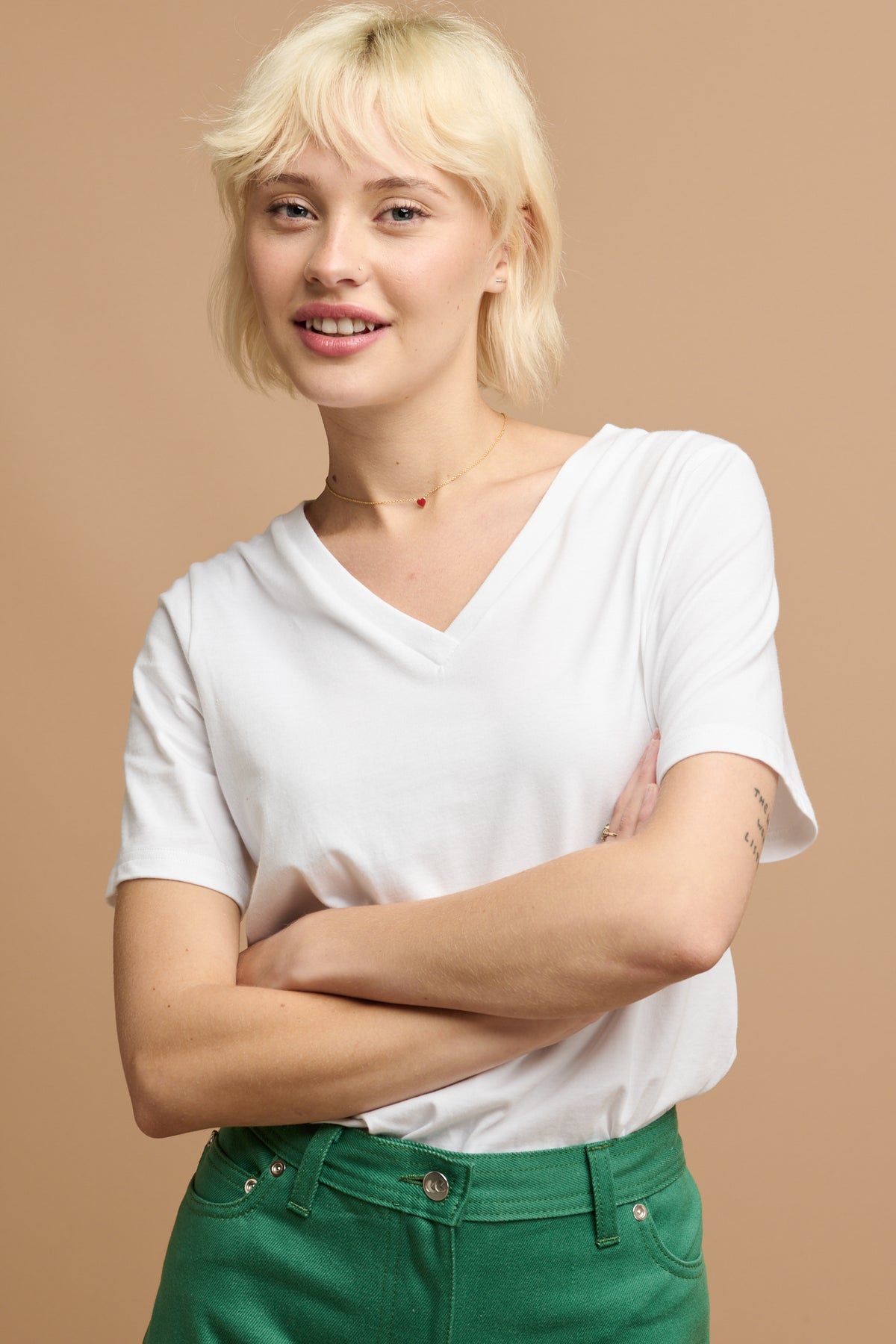 Blonde female with her arms folded wearing community clothing v neck short sleeve t shirt in white