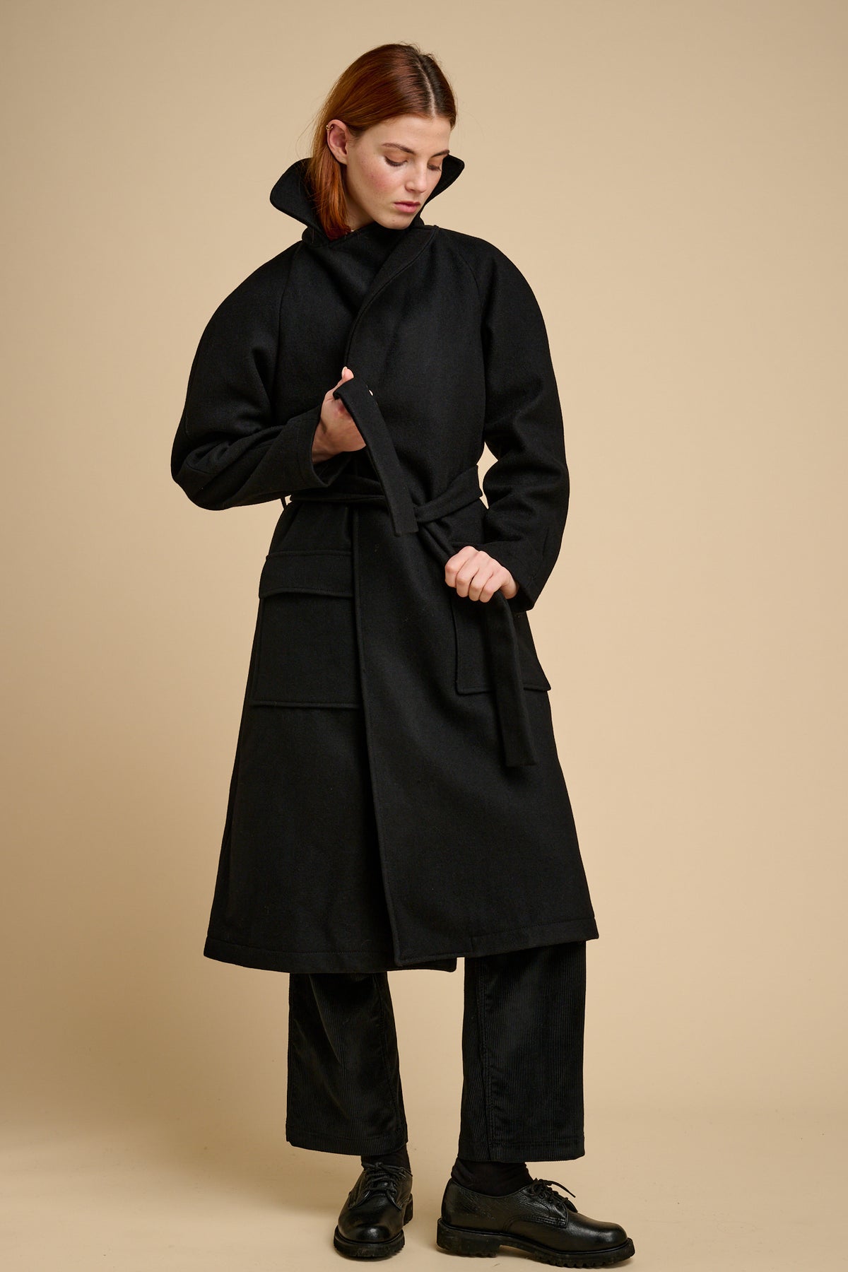 Woman wearing a black wool coat on a beige background