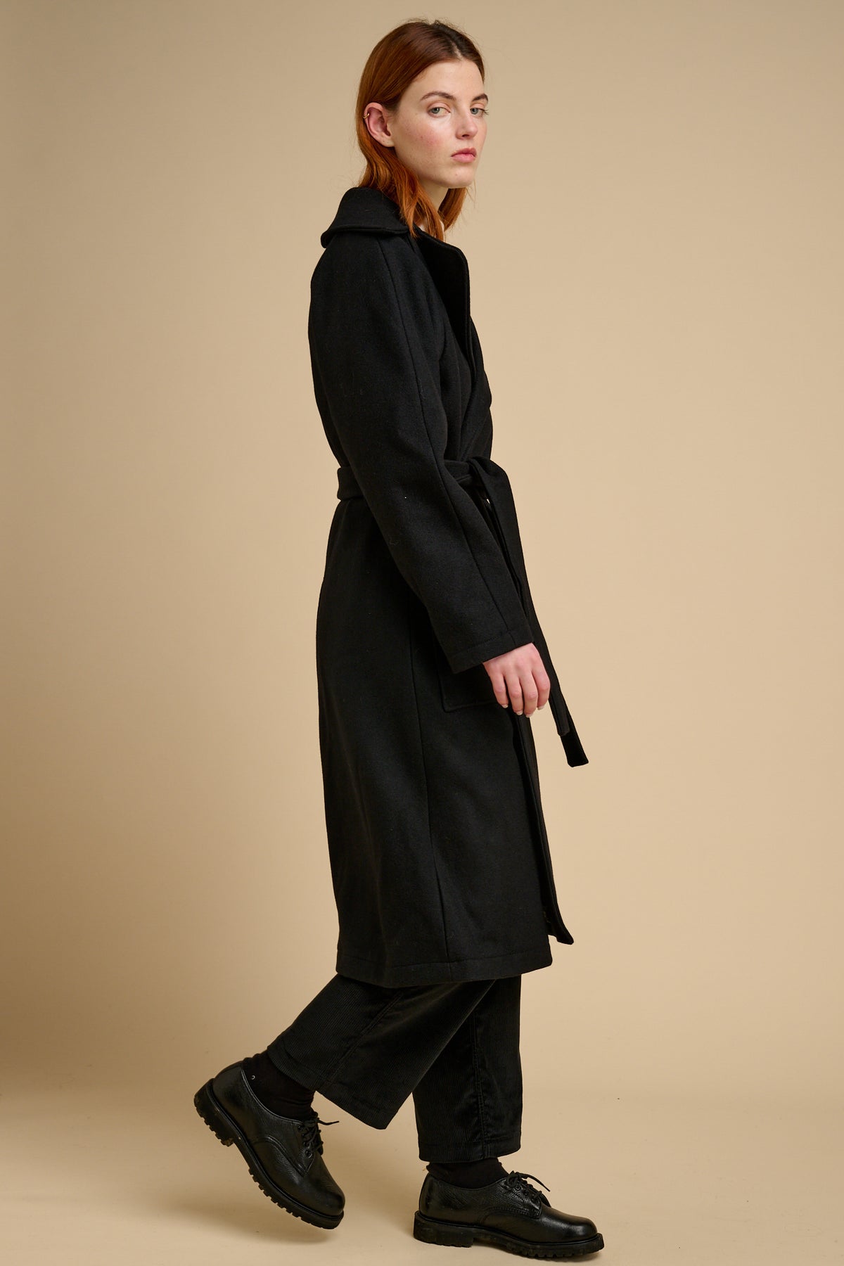Person wearing a black coat on a beige background