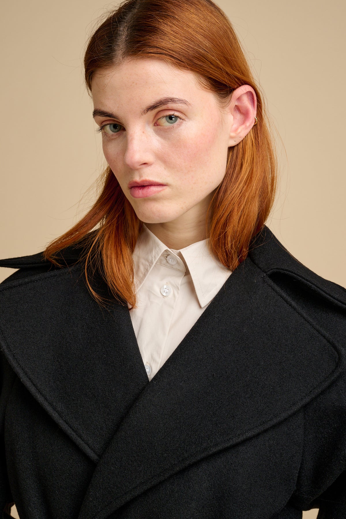 Woman wearing a black coat over a white shirt against a beige background