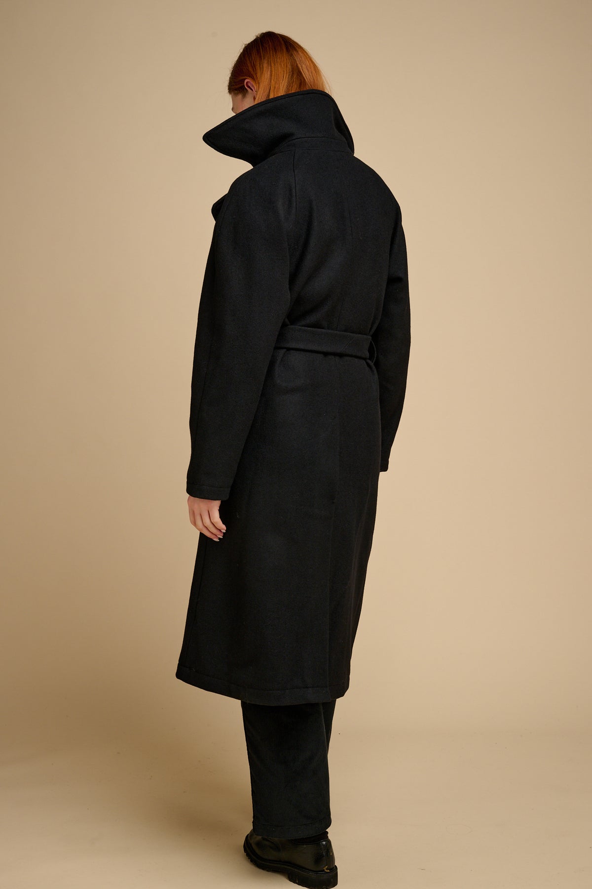 Person wearing a black coat against a beige background.