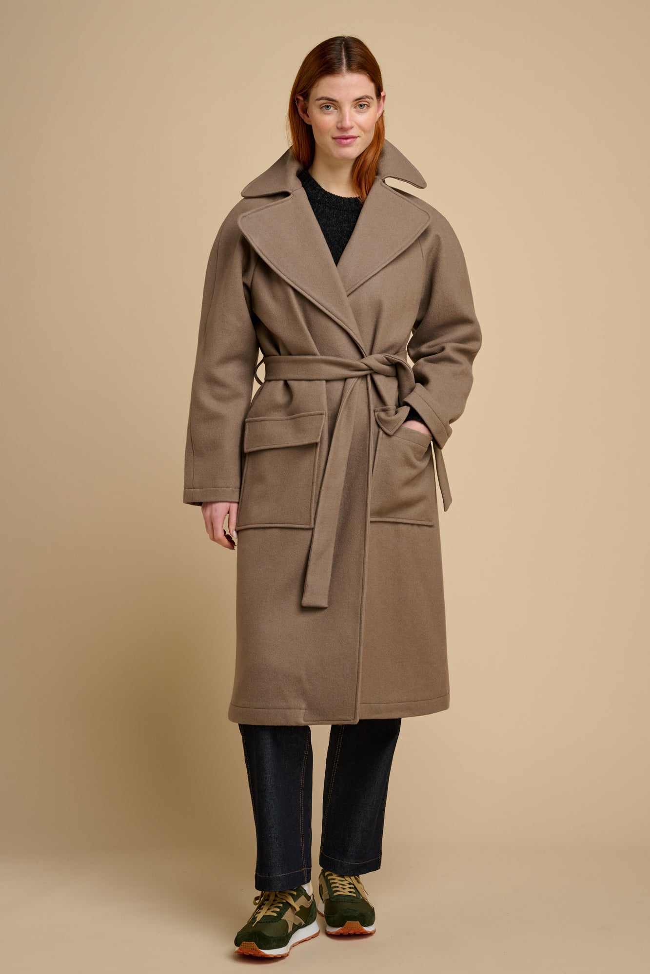 Woman wearing a beige long wool coat against a beige background