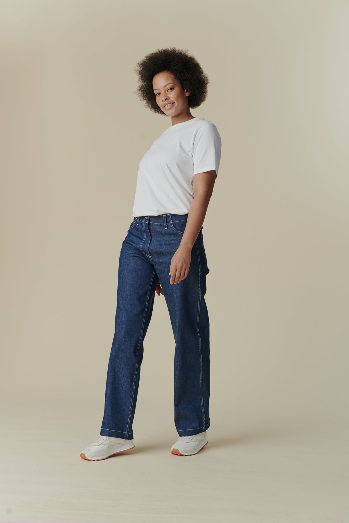 
            Female with afro wearing white crew neck white t shirt paired with wide fit women&#39;s work jean in Blue, white contrast stitching 