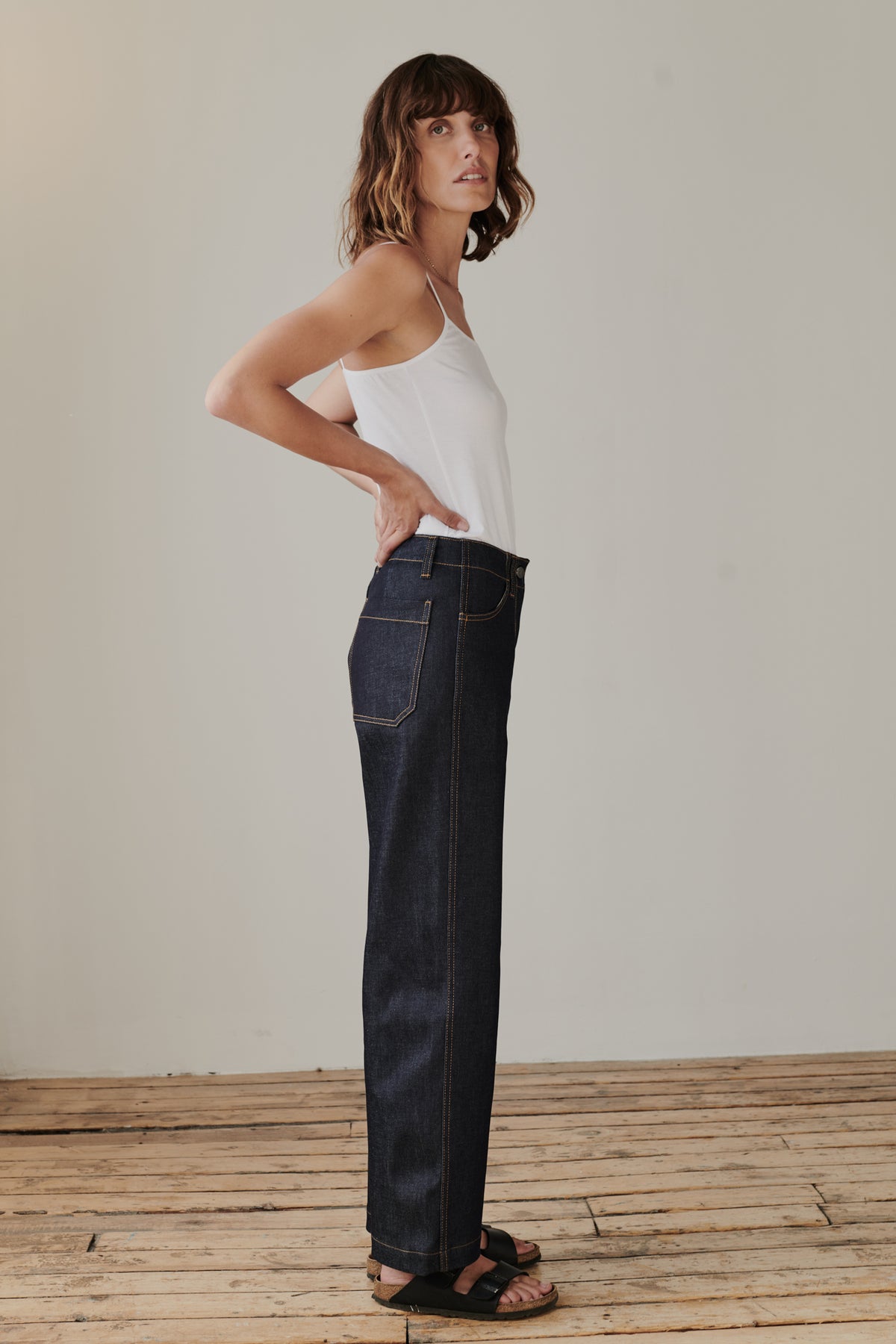 Full body side image of brunette female wearing work jean in indigo.