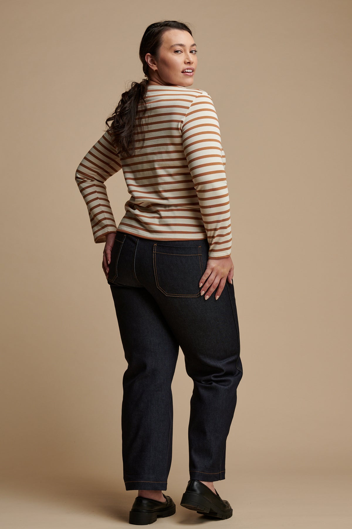 The back of female with long brown hair tied back into a low ponytail wearing work wide straight jean in indigo paired with Breton top in ecru-cinnamon.
