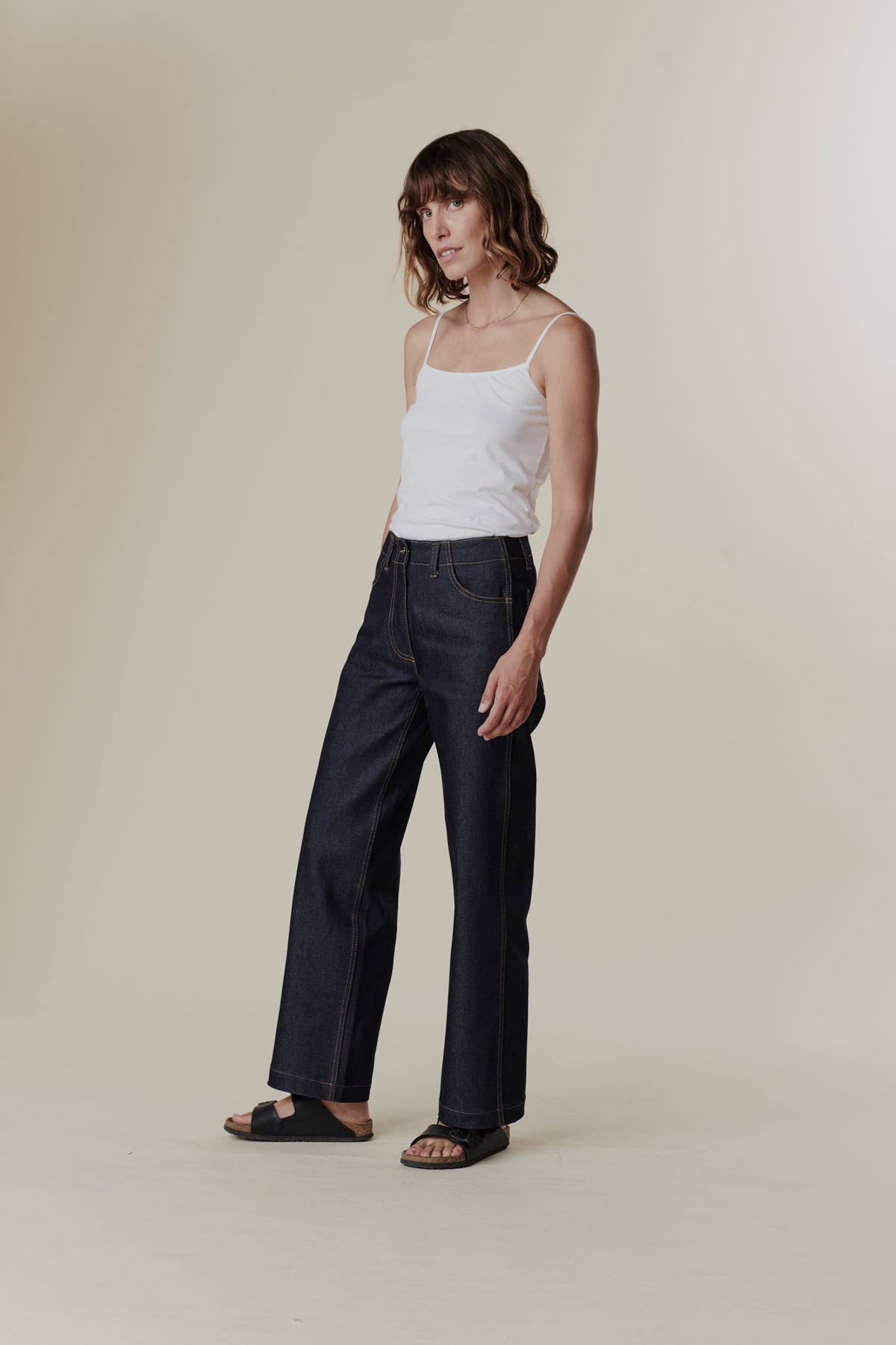 The front of female with wavy brunette bob wearing work jean in indigo paired with white camisole