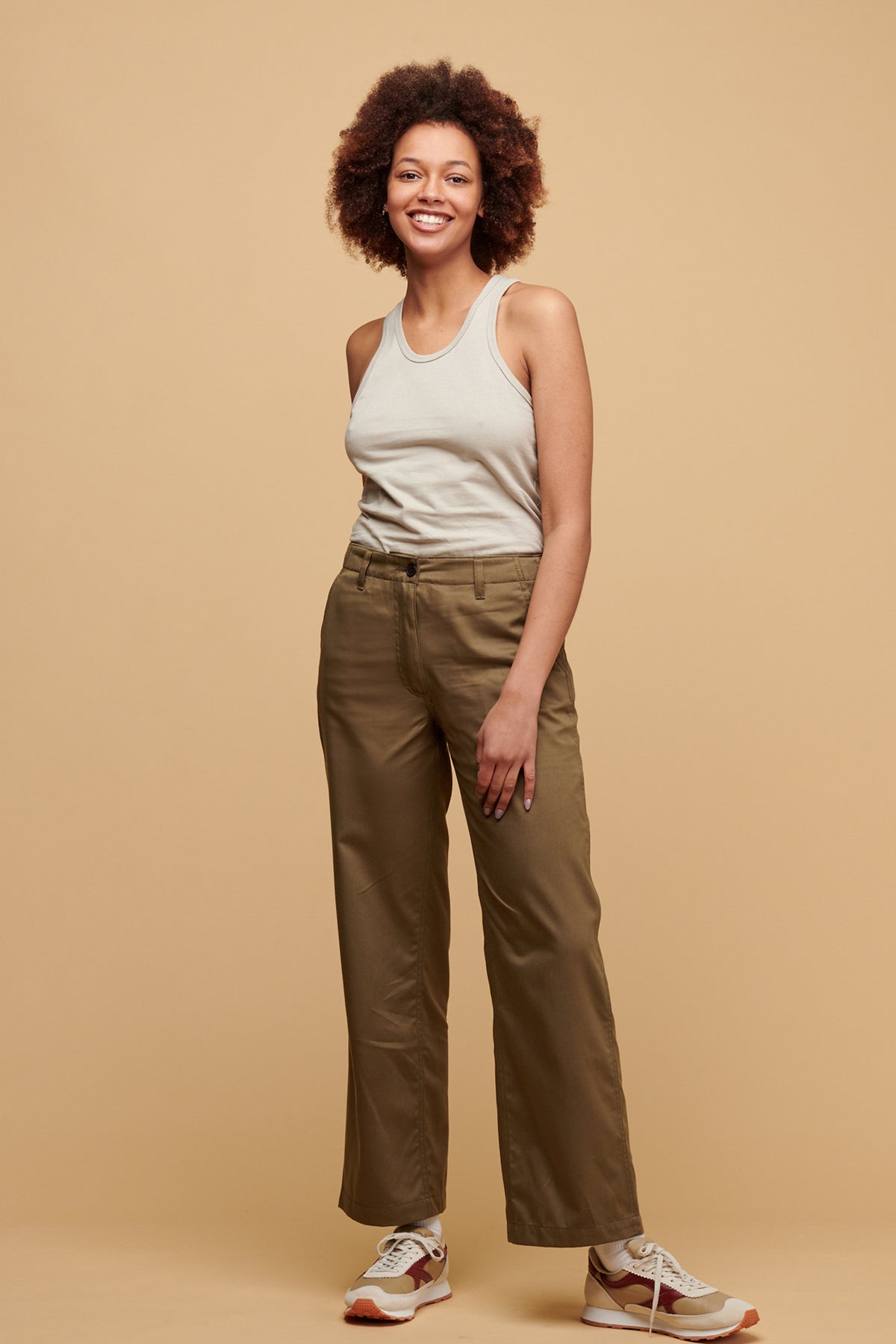 
            Female wearing work trousers in light olive paired with racer back vest in stone tucked into the trousers and Beacon trainers in neutral