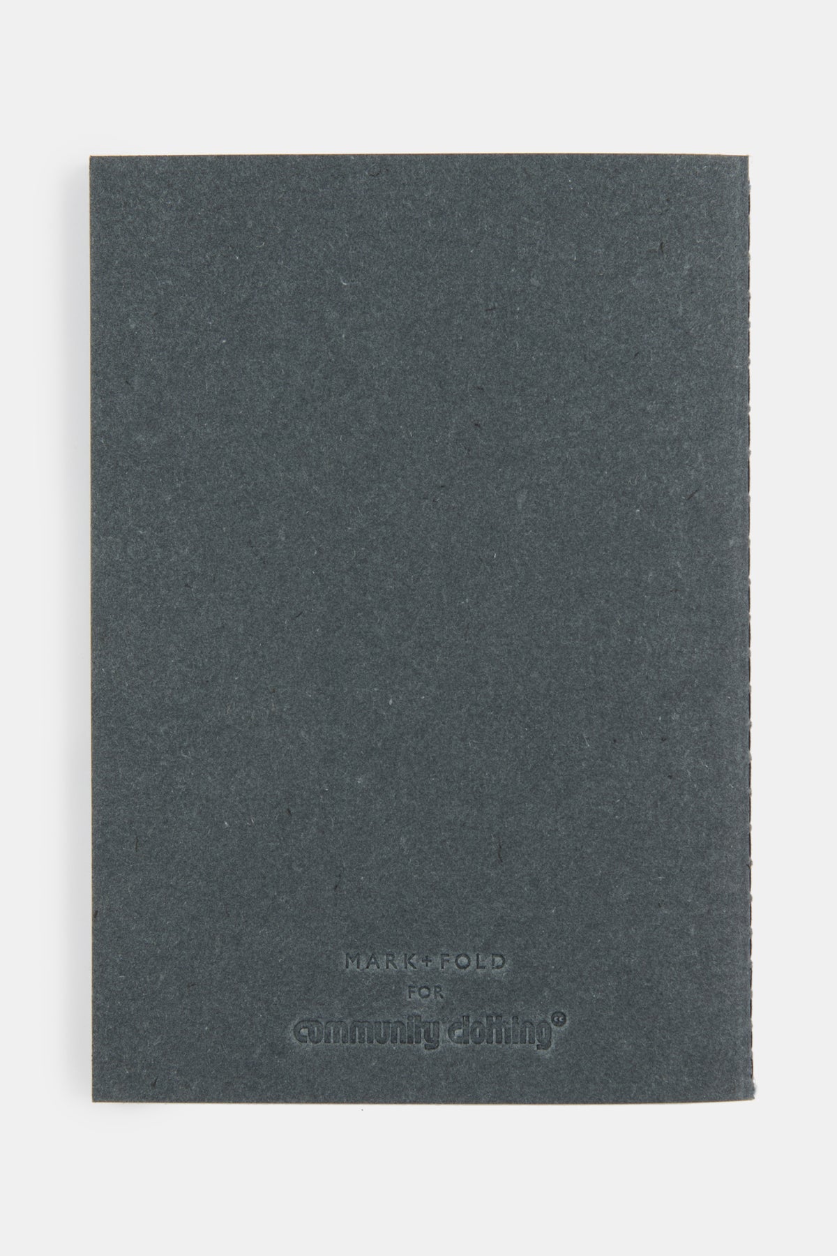 
            The back of recycled denim notebook in black with embossed Mark + Fold for Community Clothing logo.