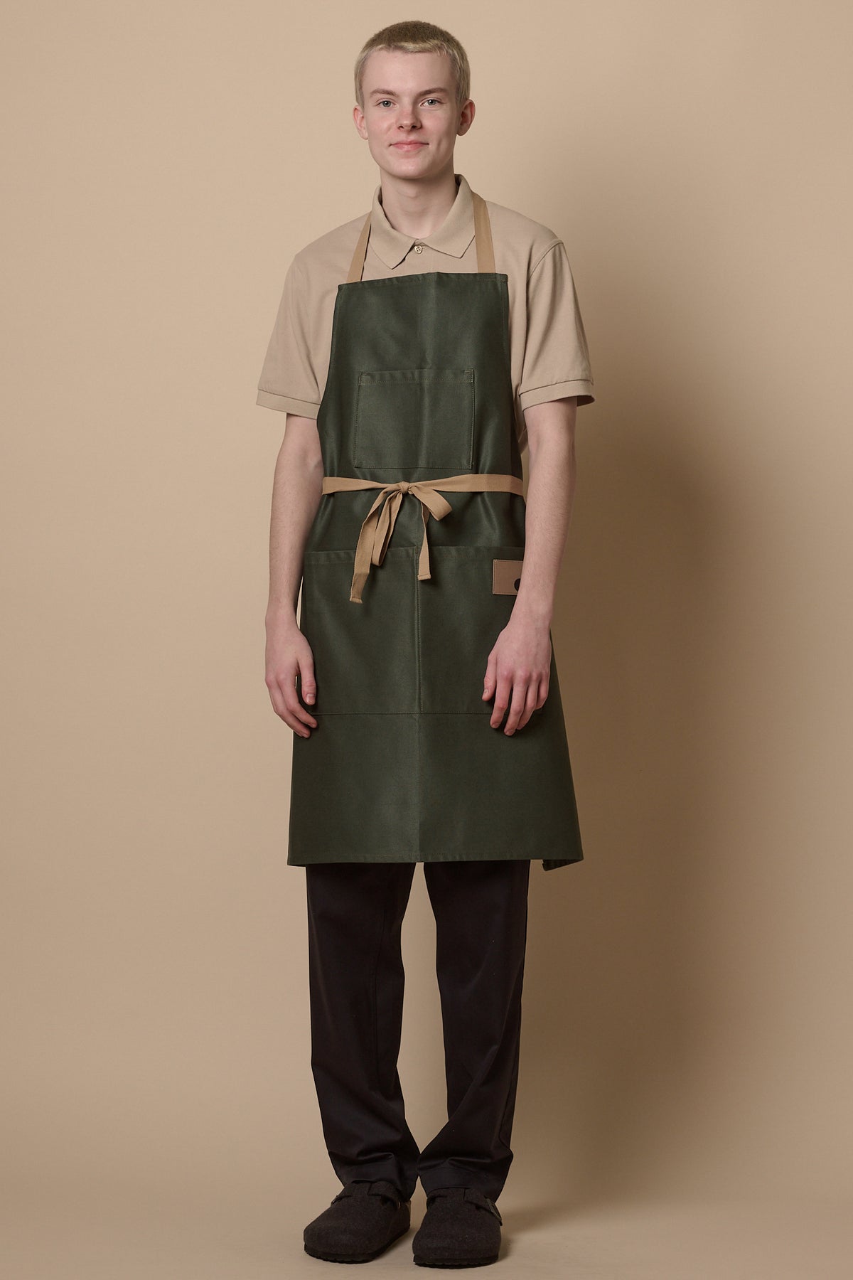 
            Male wearing apron in forest green tied at the front. 3 front pockets with CC logo patch