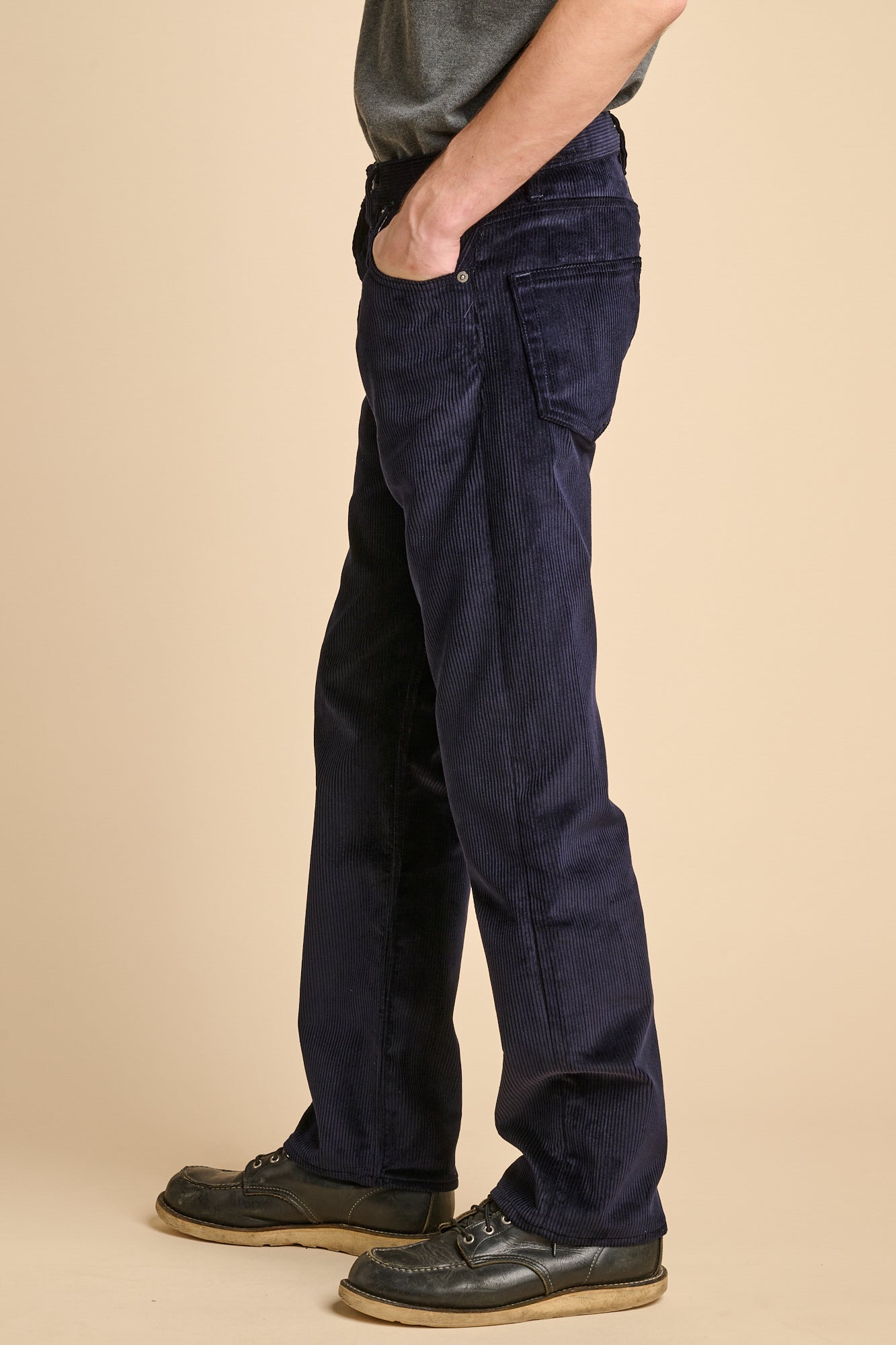 The side of man wearing navy corduroy straight leg jeans with black shoes.