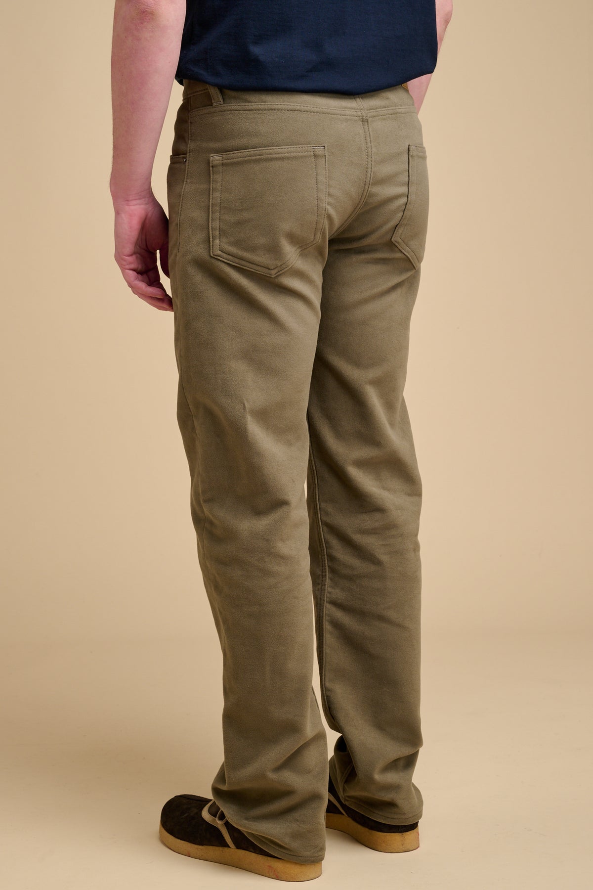The back of male wearing olive moleskin jeans on beige background.